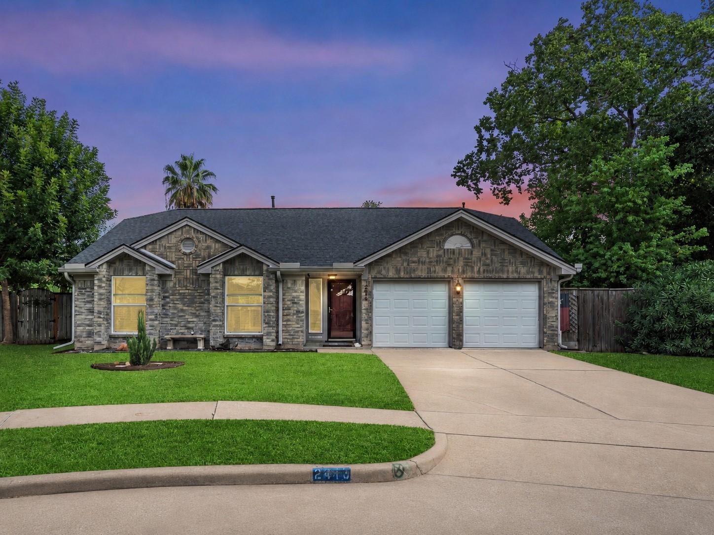 Stone-front home with a two-car garage and curved driveway at dusk.