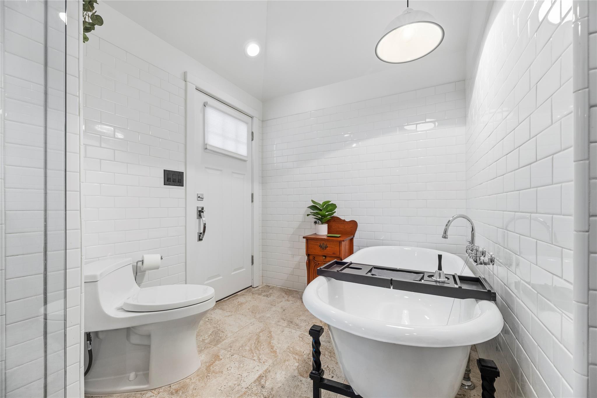 White subway-tile bathroom with a freestanding tub, black bath tray, and glass shower partition.
