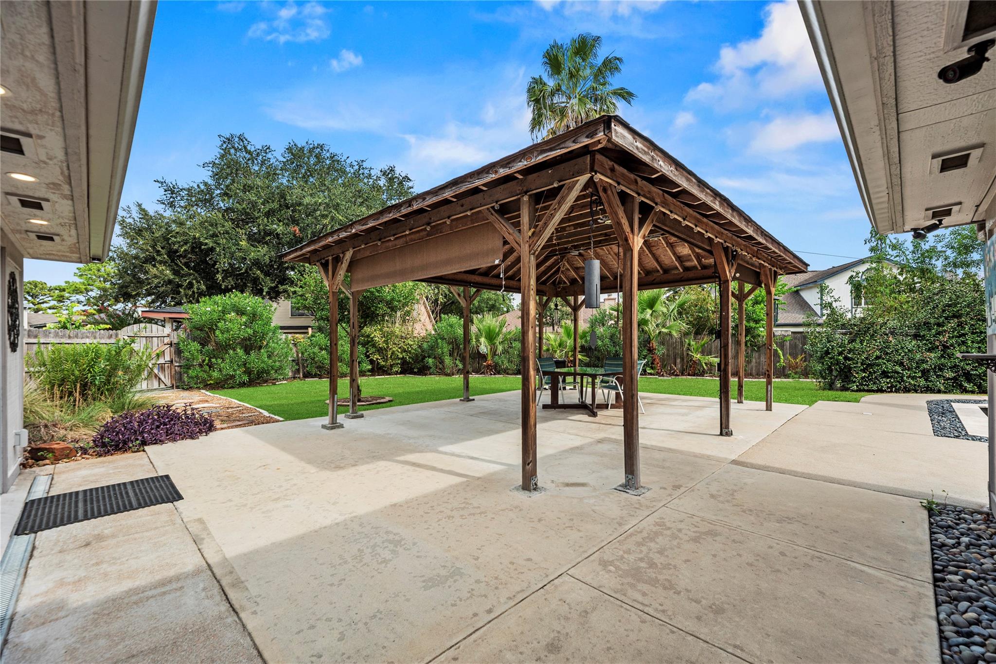 Backyard patio with a timber pavilion, outdoor dining set, concrete paving, and landscaped lawn.