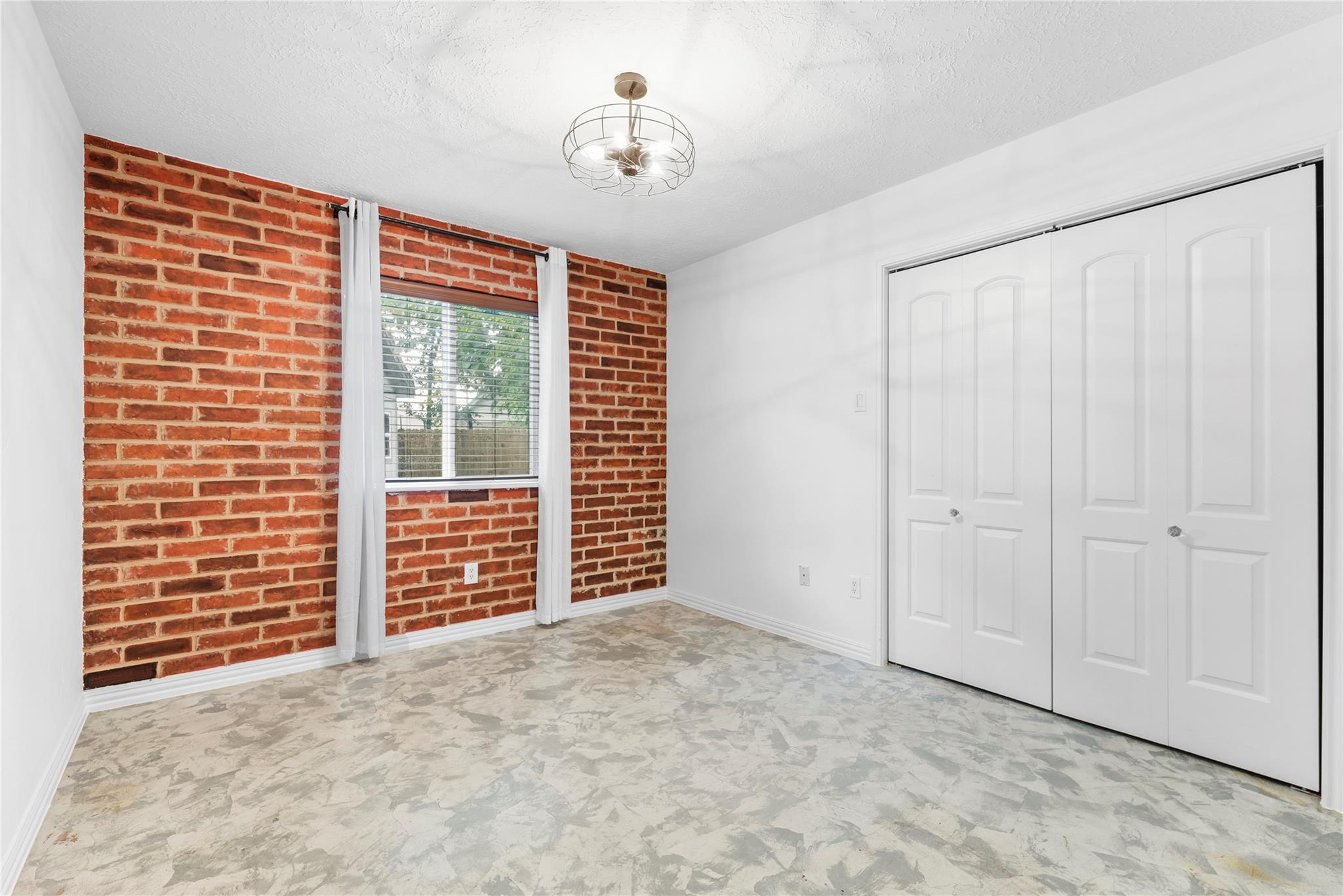 Empty bedroom with a red brick accent wall, curtained window, and wide closet doors.