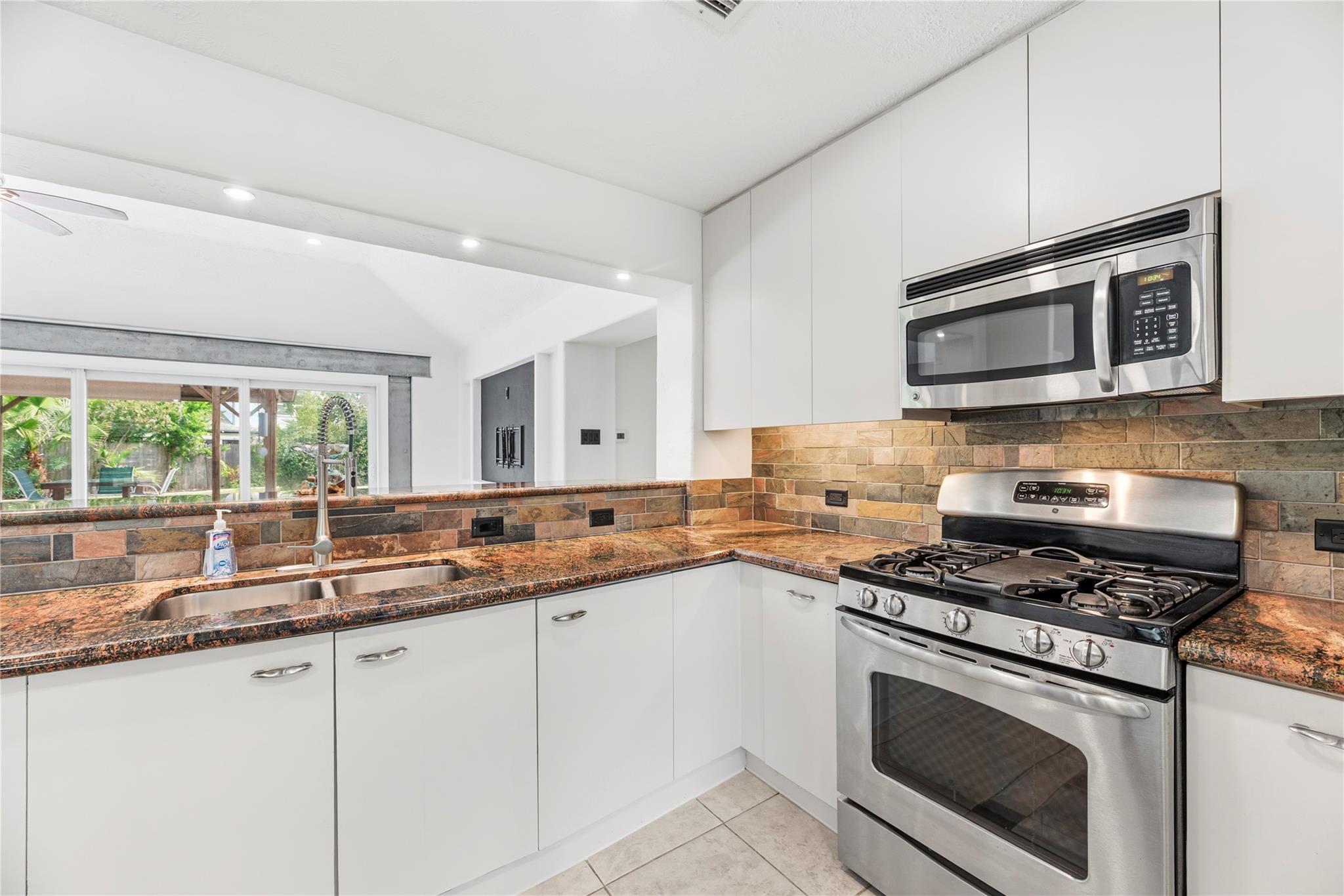 Kitchen with white cabinets, granite counters, stone backsplash, and stainless steel gas range beneath a microwave.
