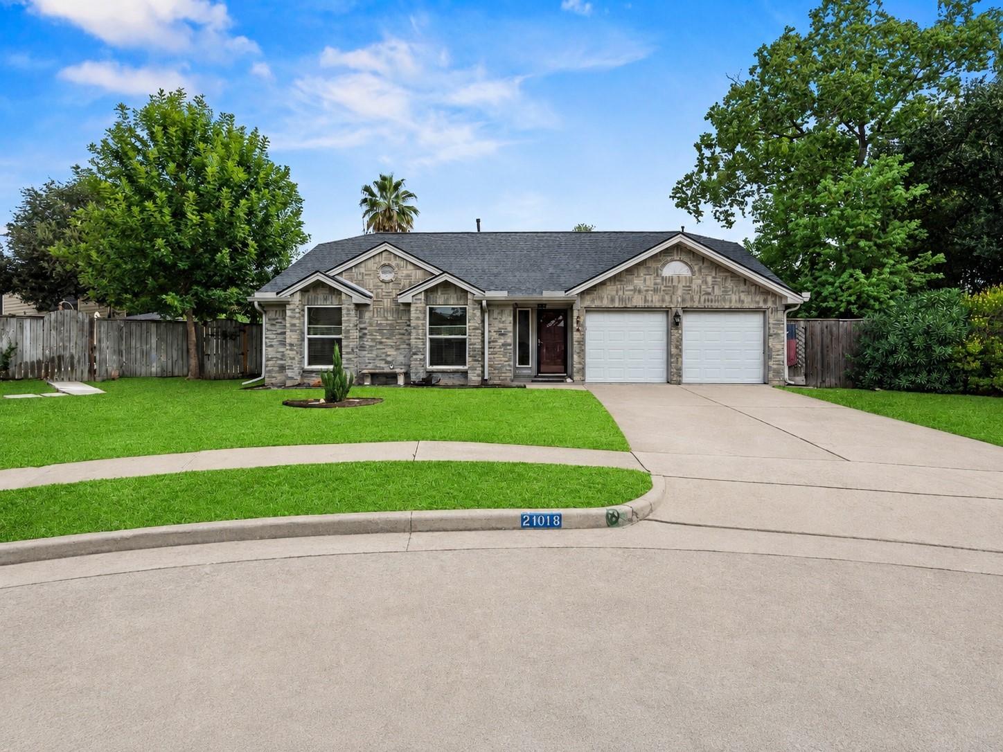Single-story stone-faced house with a two-car garage, broad driveway, and green front lawn.