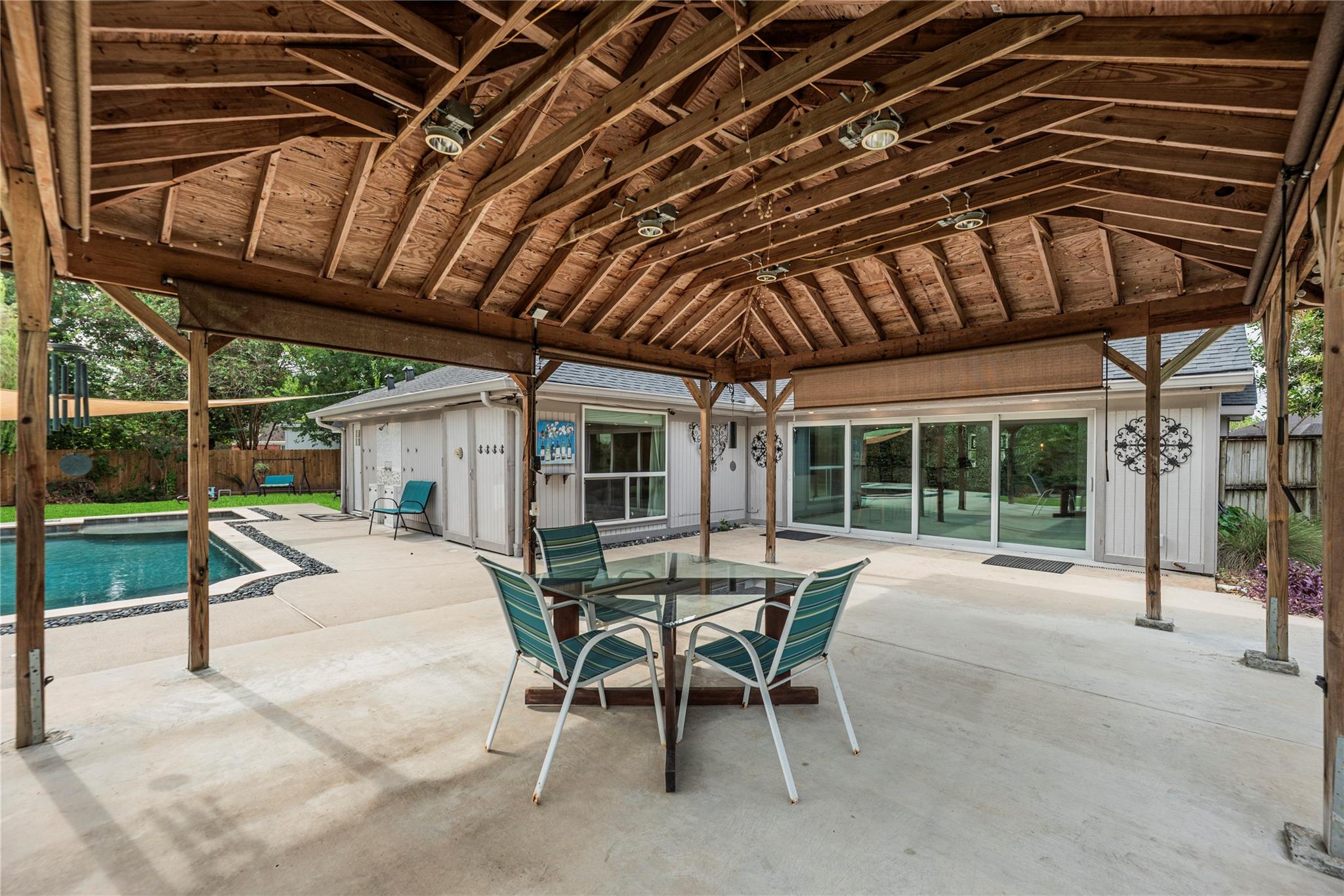 Covered timber patio with outdoor dining set beside the pool and sliding glass doors.