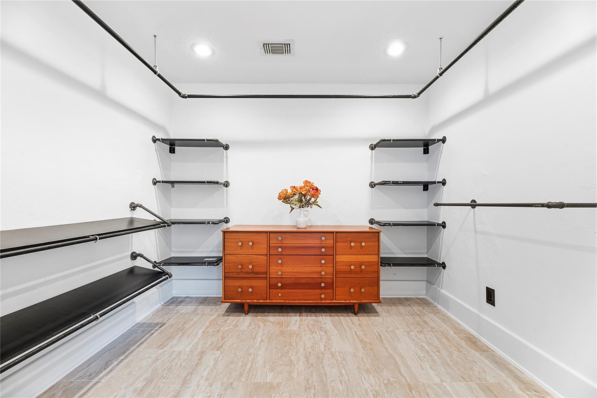 Walk-in closet with black metal shelving and a wooden dresser topped with flowers.