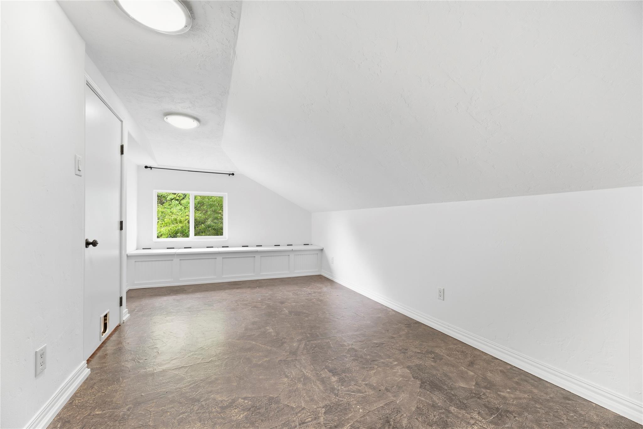 Empty room with a sloped ceiling and built-in window bench with storage beneath.