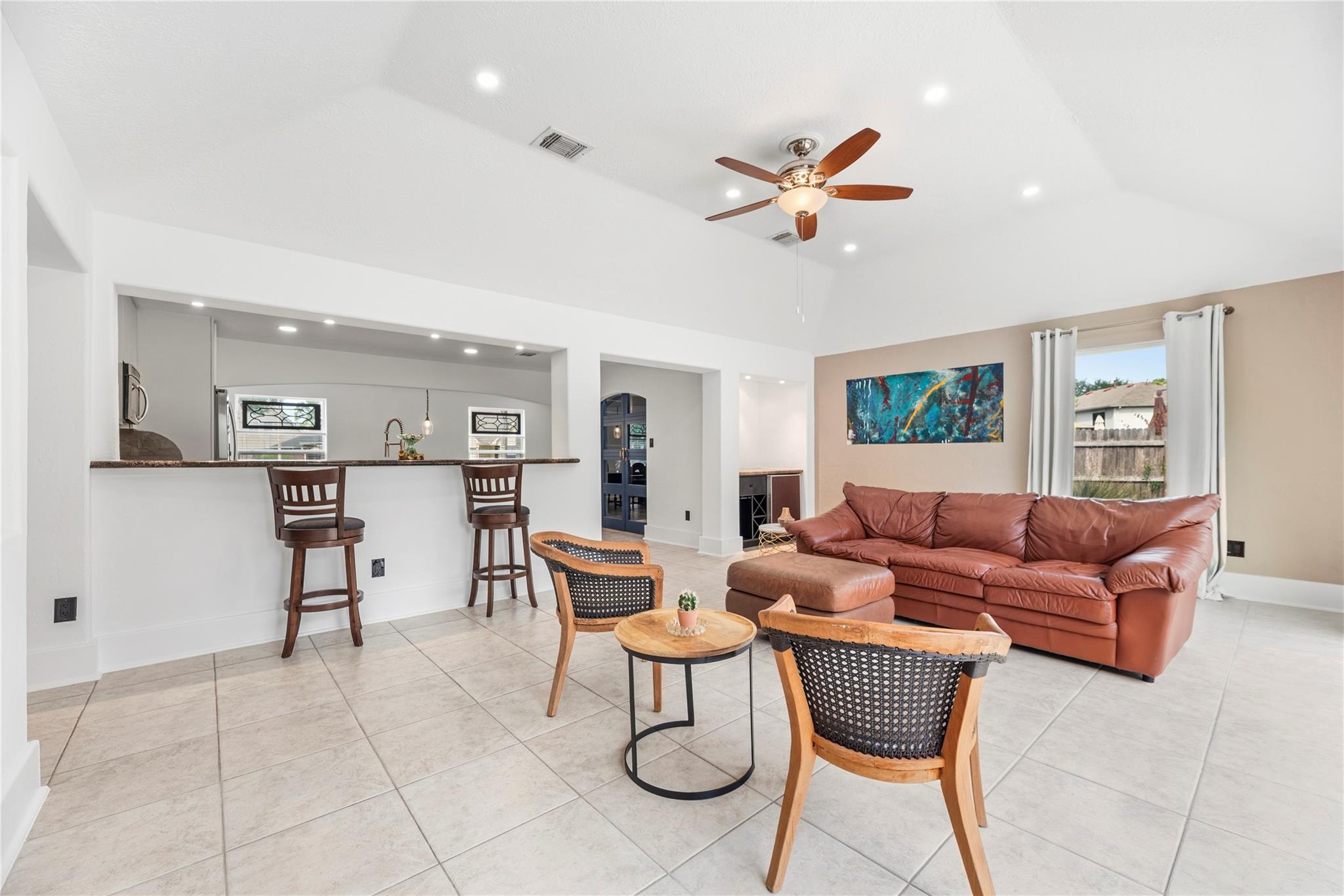 Furnished living room with a leather sectional, woven chairs, and an open kitchen breakfast bar.