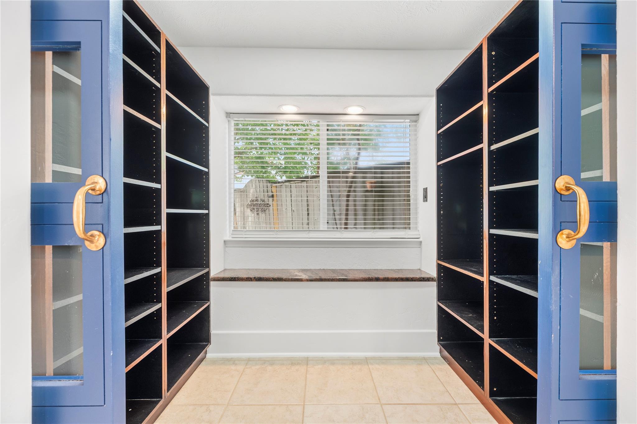 Empty room with black built-in bookshelves, blue doors, and a window with blinds.