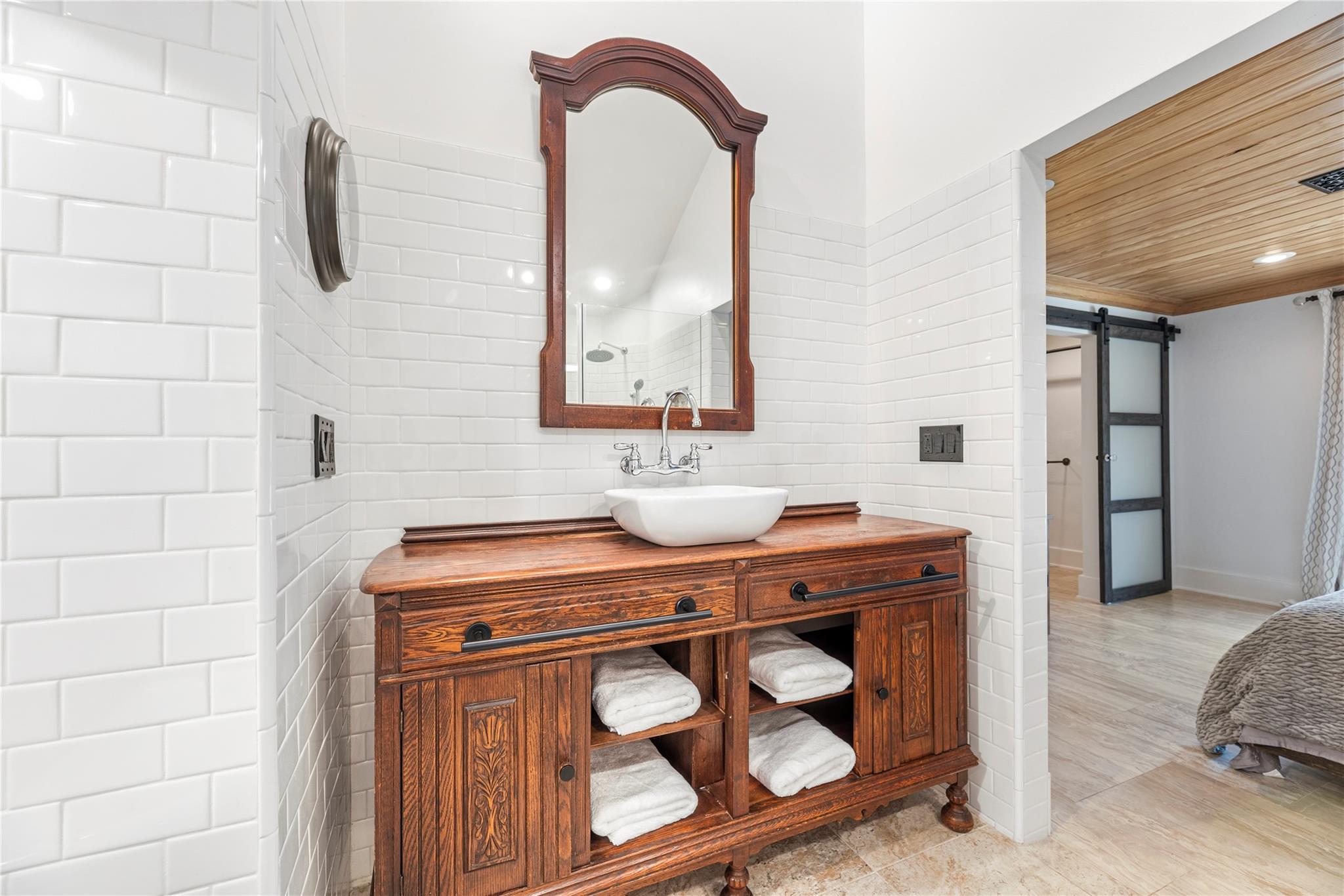 Bathroom with a carved wooden vanity, white vessel sink, arched mirror, and subway tile.