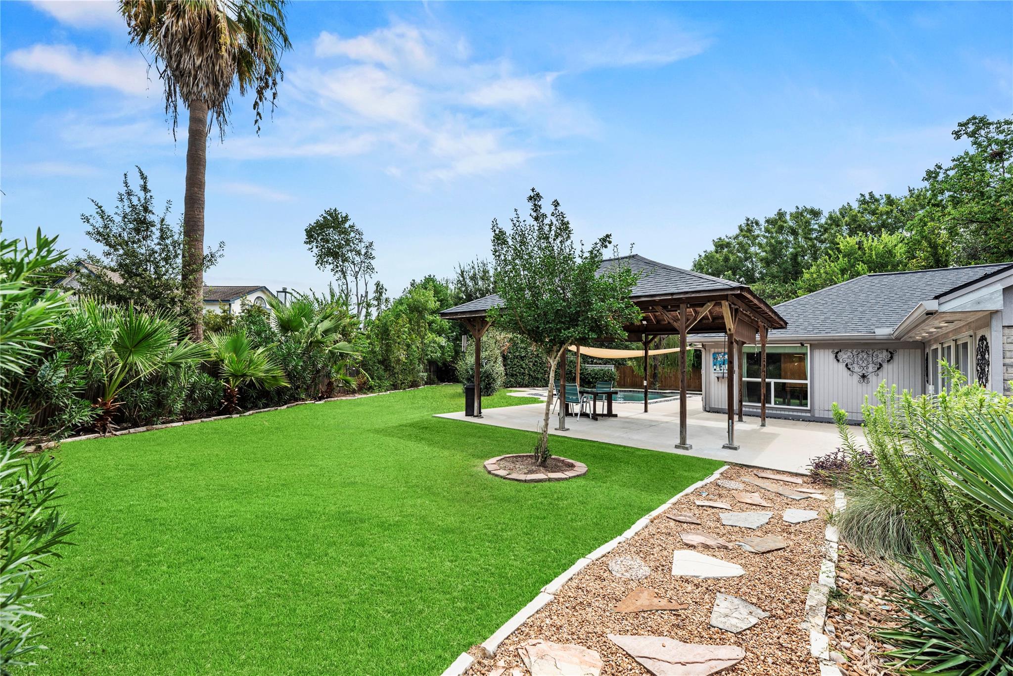 Backyard with a wooden pergola, outdoor dining set, landscaped lawn, and swimming pool.