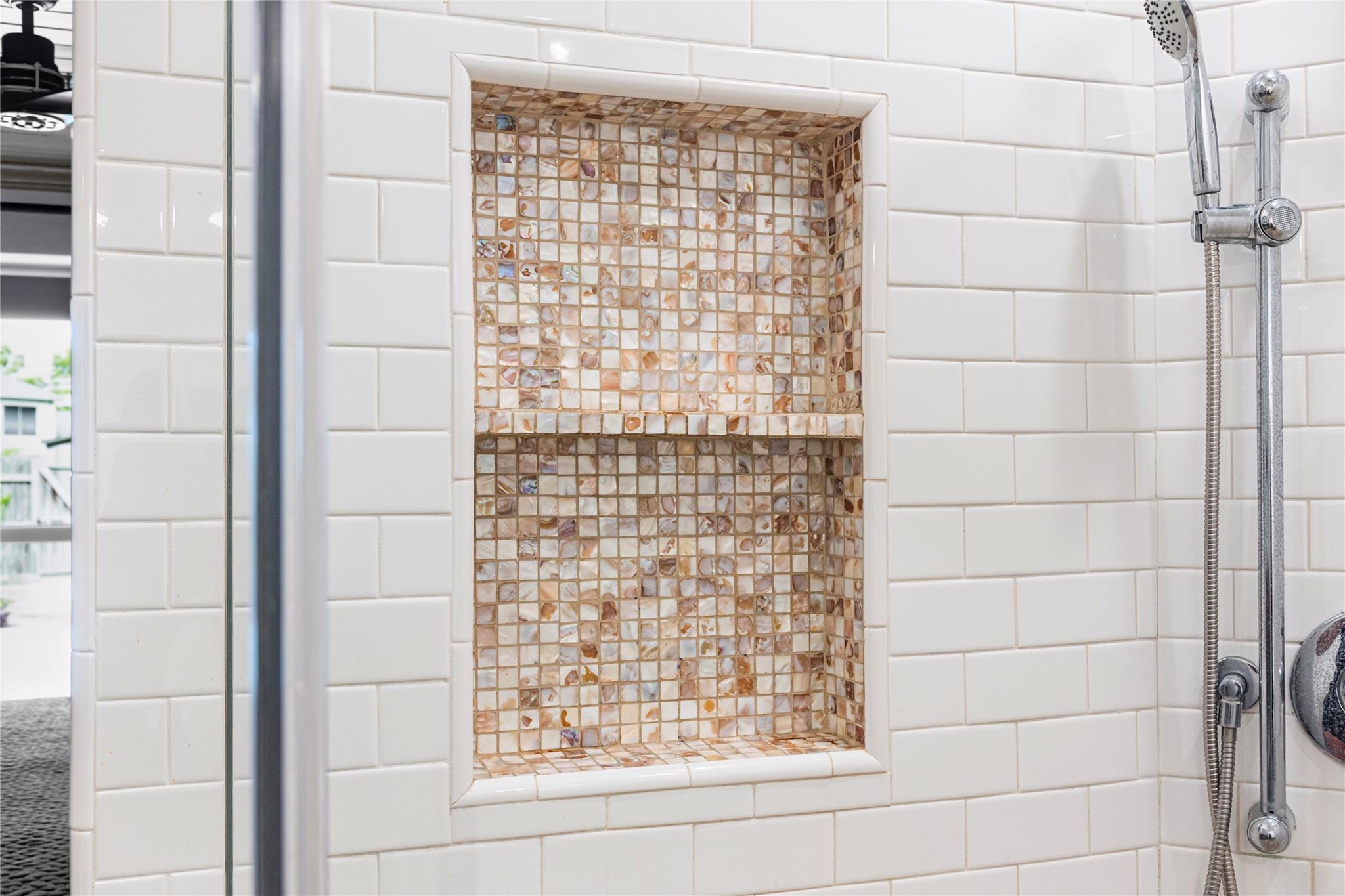Walk-in shower with a warm-toned mosaic tile niche and chrome handheld showerhead