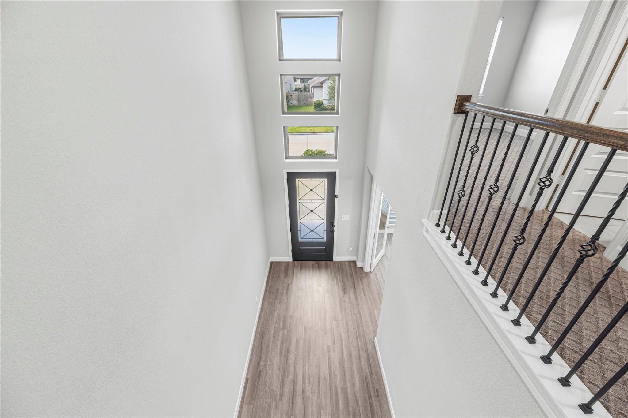 Two-story foyer with stacked windows above the front door and a carpeted landing with black metal railing.