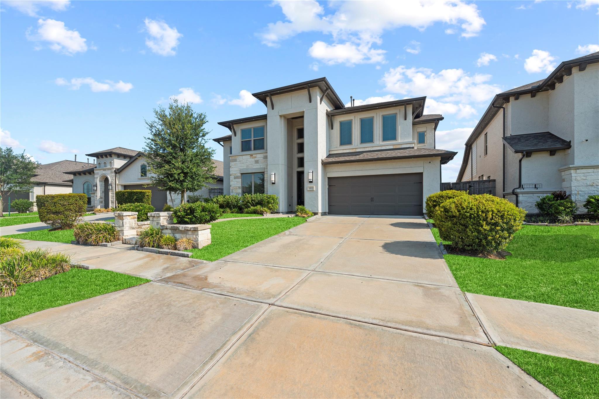 Two-story home with a dark double garage, broad driveway, green lawn, and landscaped front garden.