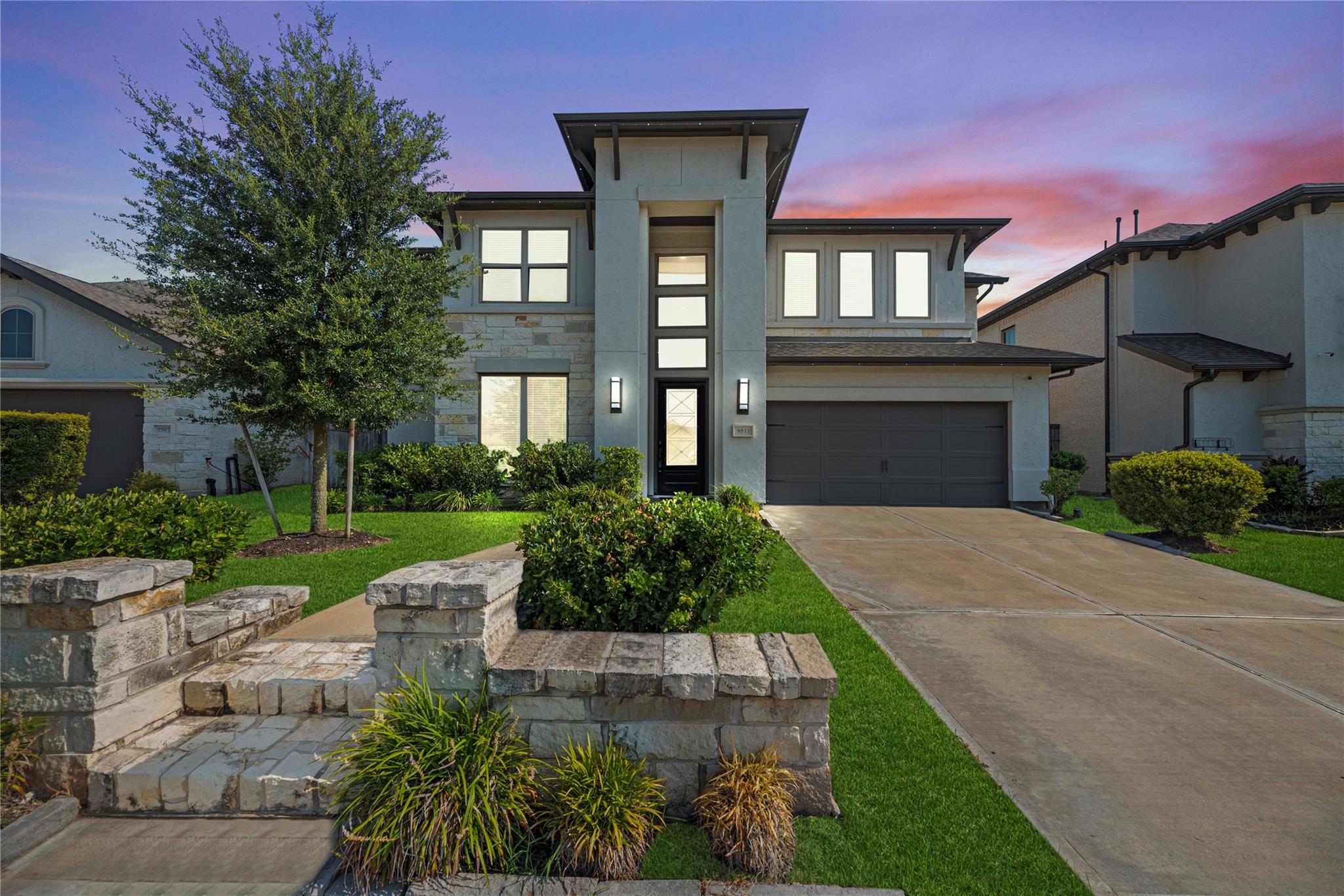 Modern two-story home with stone accents, landscaped front yard, and wide driveway at dusk.