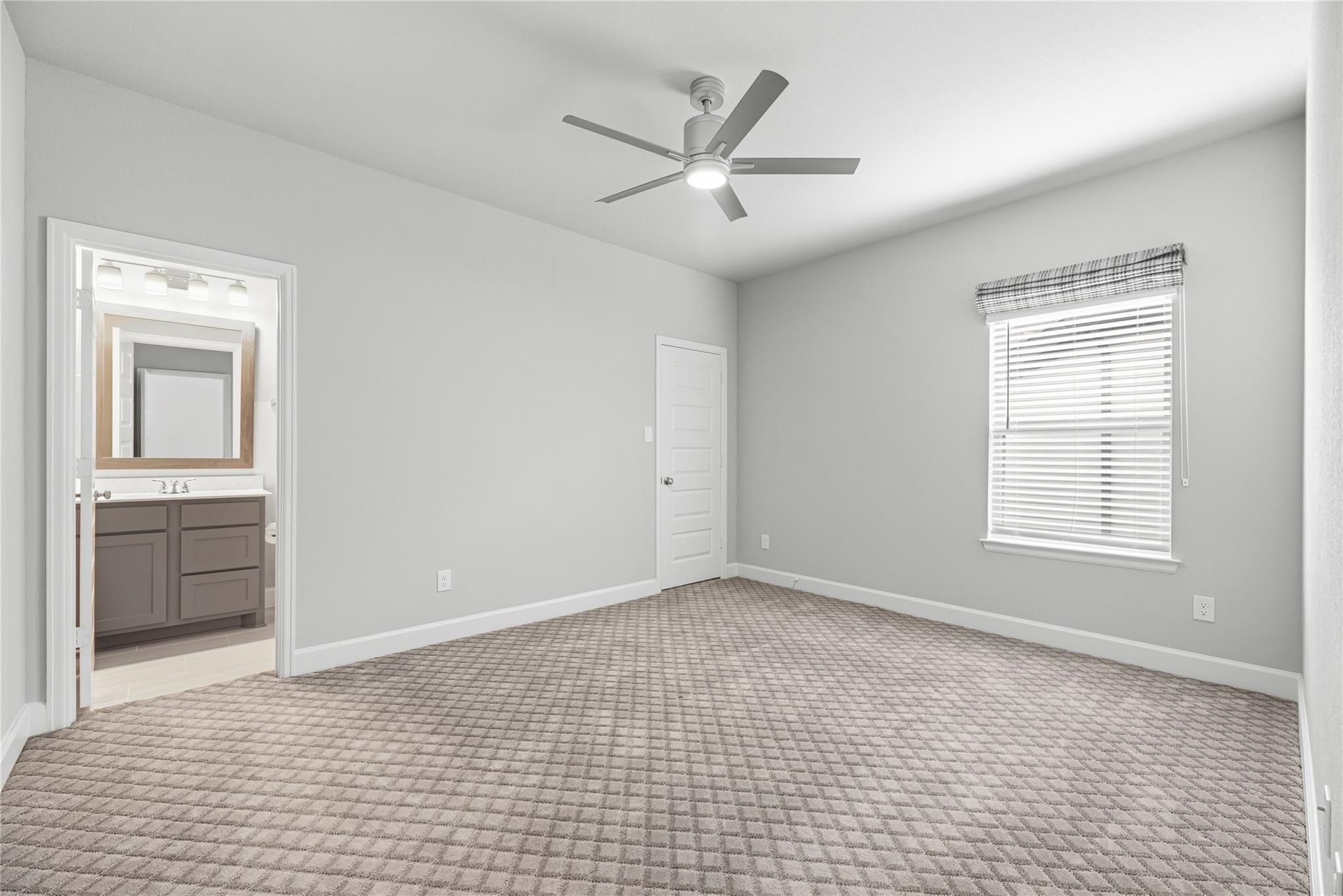 Empty bedroom with patterned carpet, ceiling fan, and doorway to a bathroom vanity.