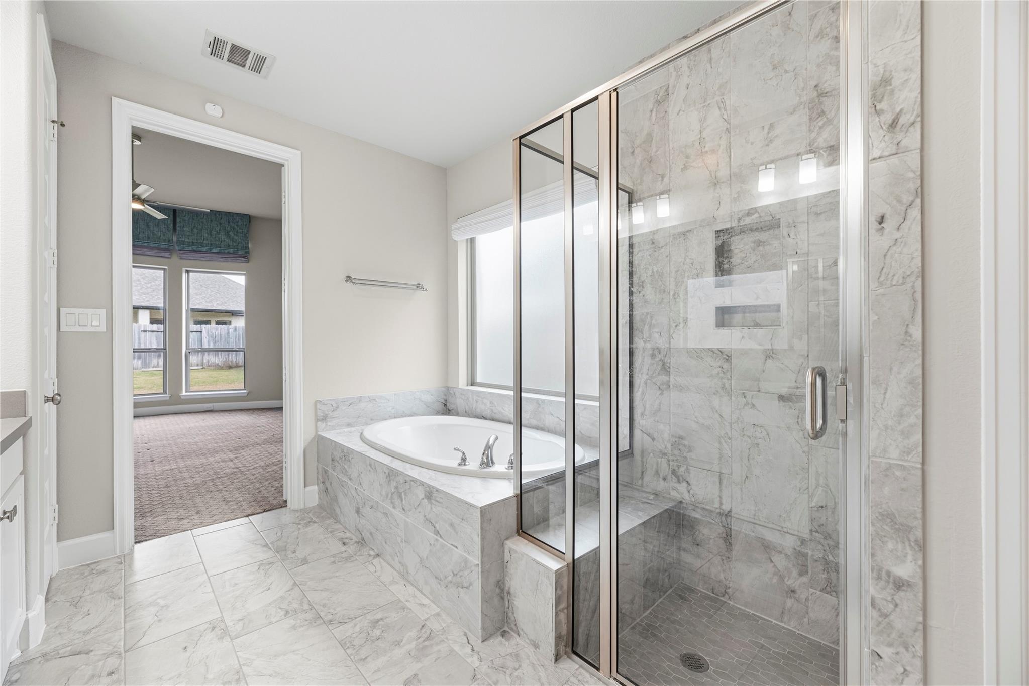 Primary bathroom with a marble-look soaking tub and glass-enclosed shower.
