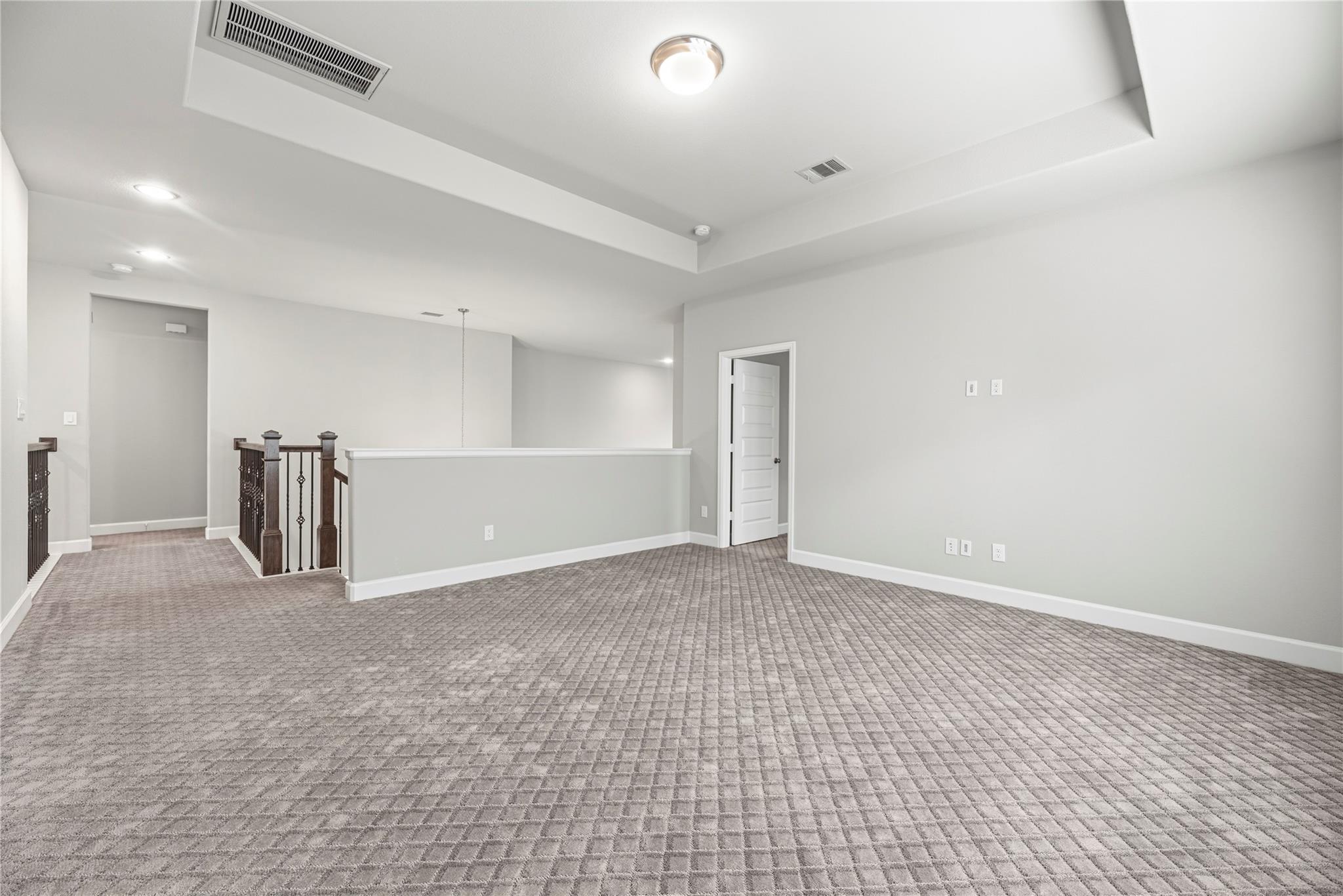 Empty upstairs loft with patterned carpet and a dark railing by the stair landing.