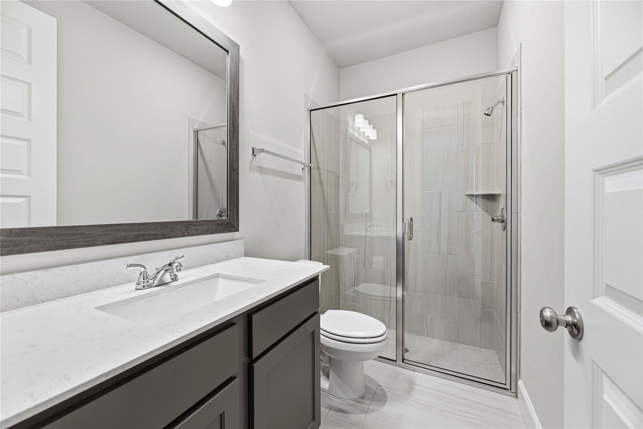 Modern bathroom with a quartz vanity, dark gray cabinets, and a glass-enclosed tiled shower.