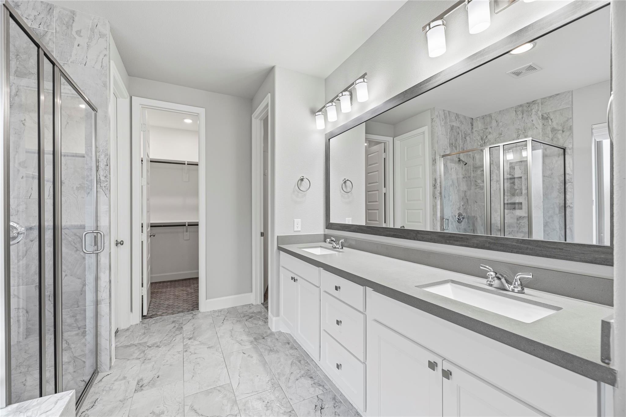 Bathroom with a long double-sink vanity, large mirror, marble-look tile, and glass-enclosed shower.