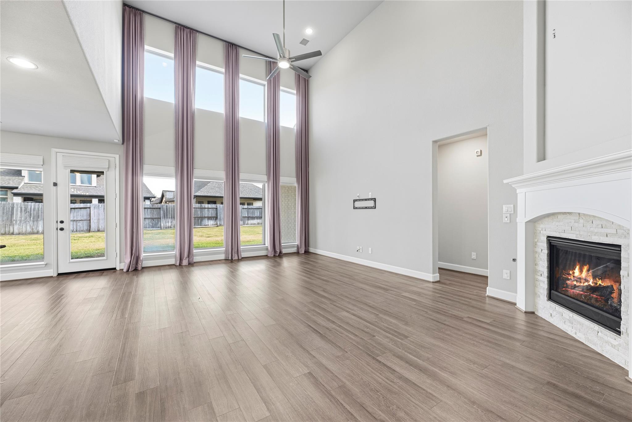 Vacant living room with tall curtained windows and a white stone fireplace.