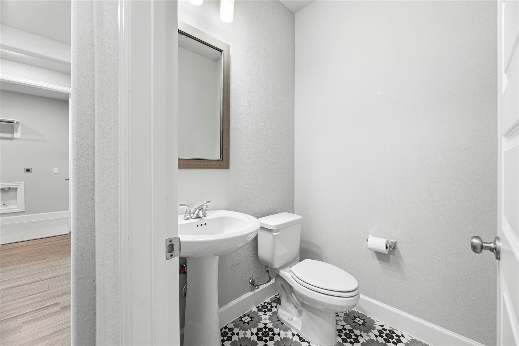 Bathroom with a pedestal sink, toilet, framed mirror, and geometric black-and-white floor tile.