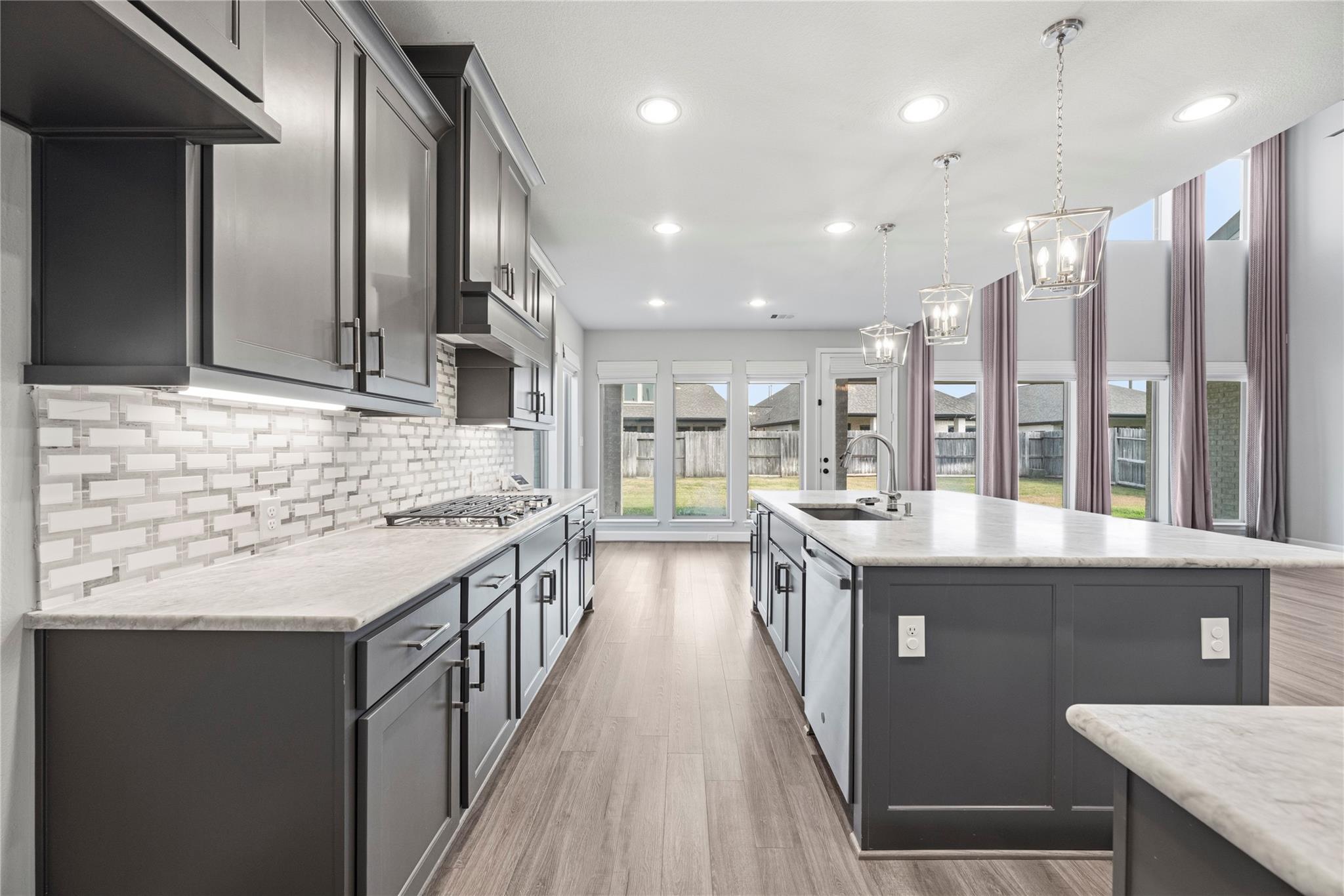 Modern kitchen with a large island, dark cabinetry, patterned backsplash, and tall windows overlooking the backyard.