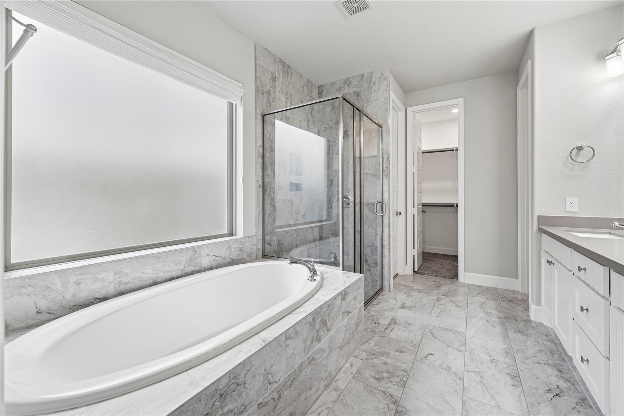 Bathroom with a marble-tiled soaking tub, glass shower, and white vanity.