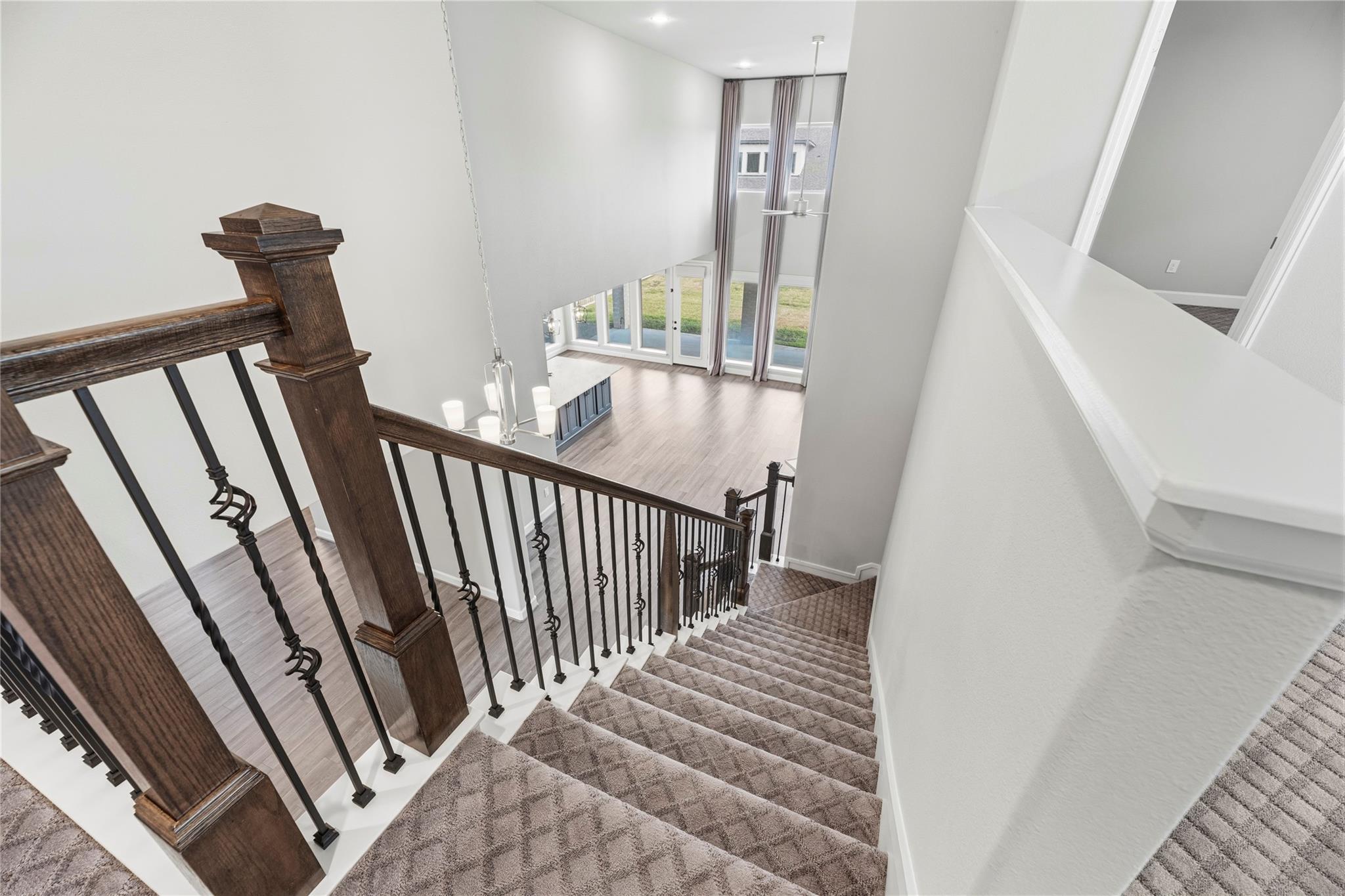 Carpeted staircase with dark wood and iron railings overlooking a bright foyer with tall windows.