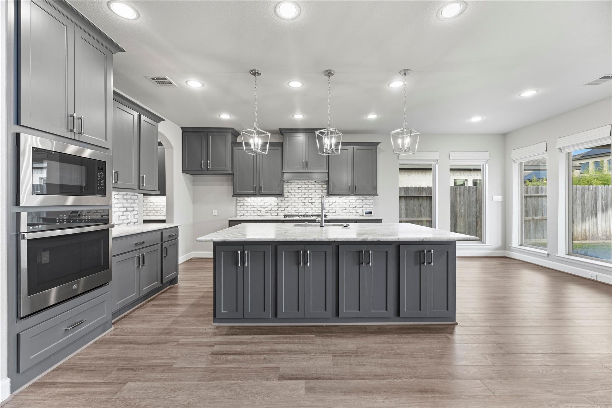 Kitchen with gray cabinets, a large island, stainless steel appliances, and windows along one wall.