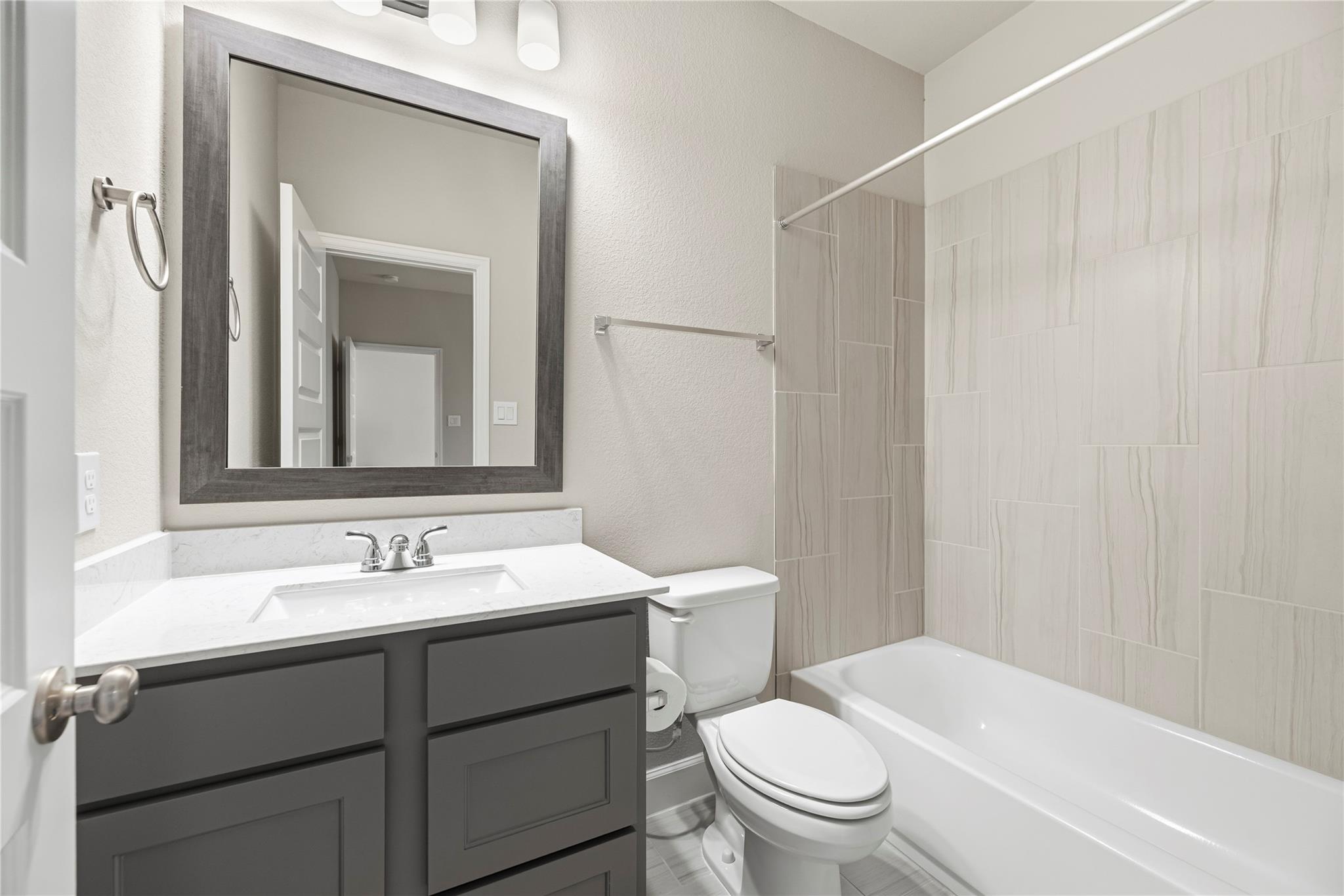 Bathroom with a dark gray vanity and a bathtub surrounded by light marble-look tile.