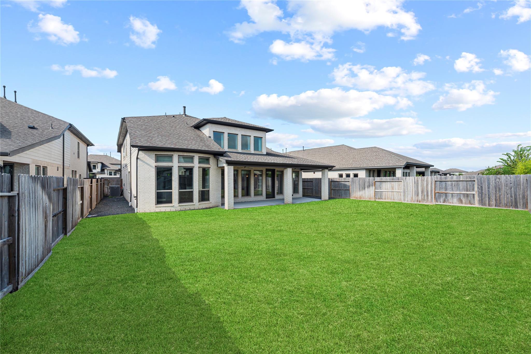 Two-story brick home with a covered patio and wide fenced backyard lawn.