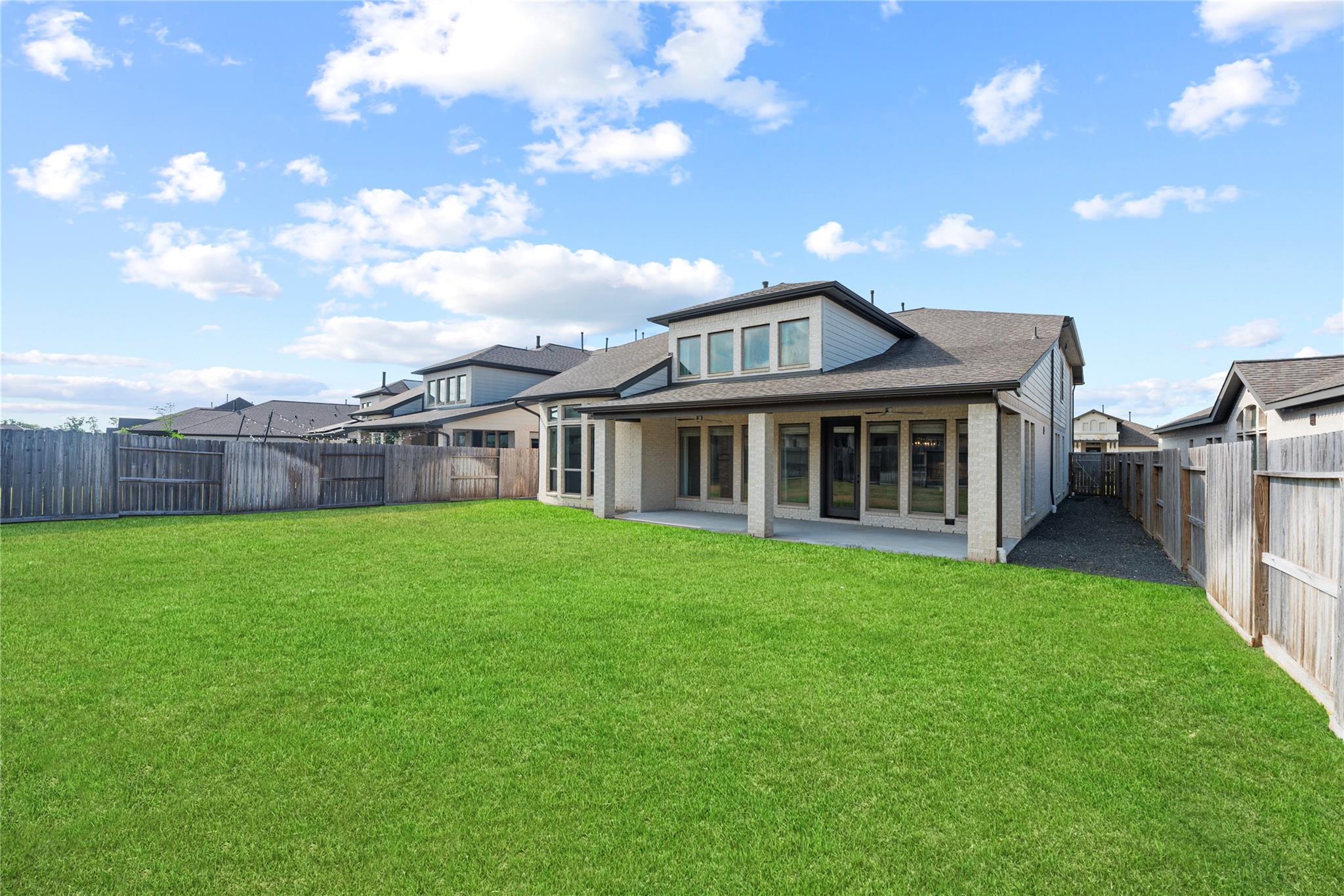 Rear of a two-story house with a covered patio and broad fenced lawn.