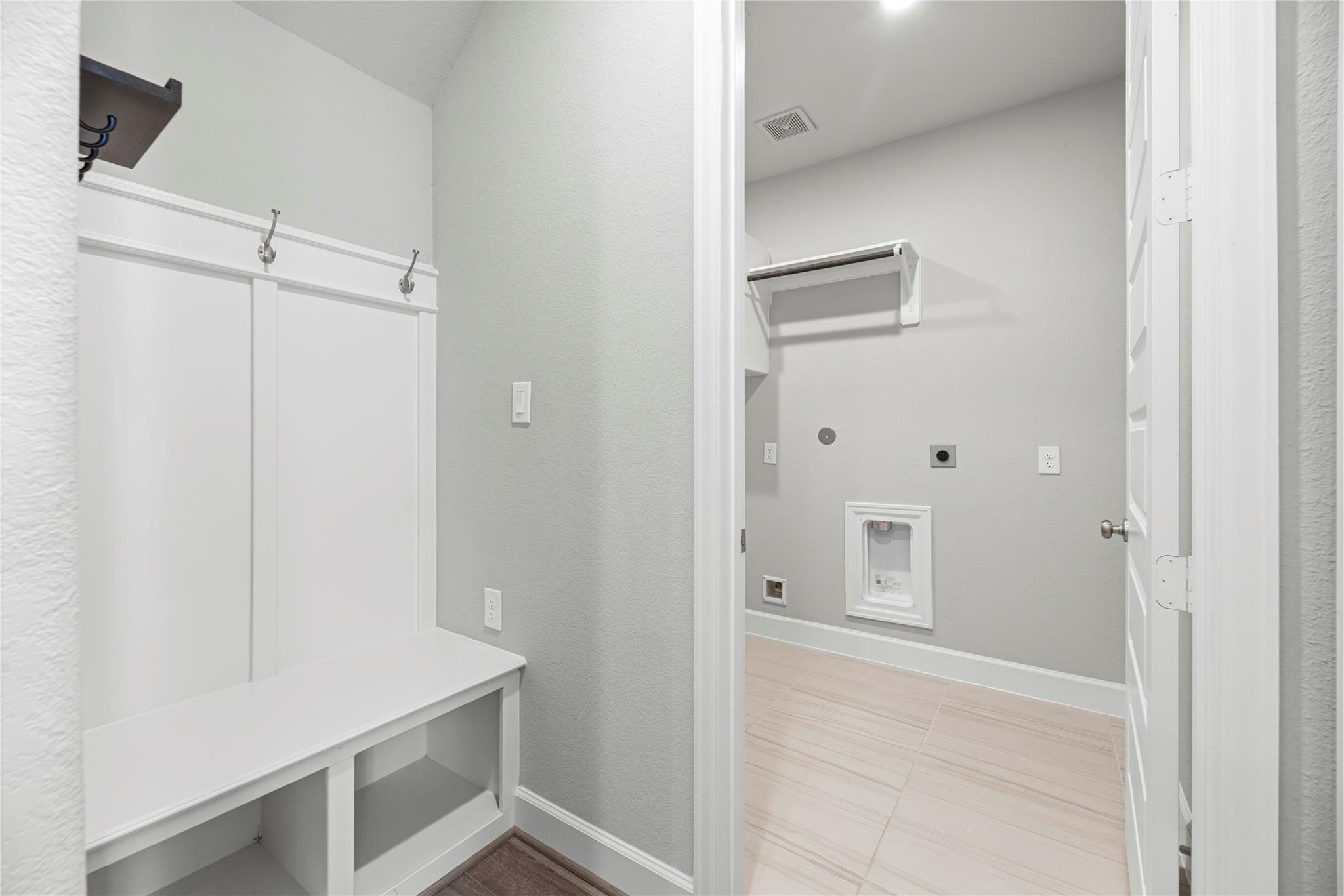 Laundry room with washer hookups, tiled floor, and an adjacent built-in bench with coat hooks.