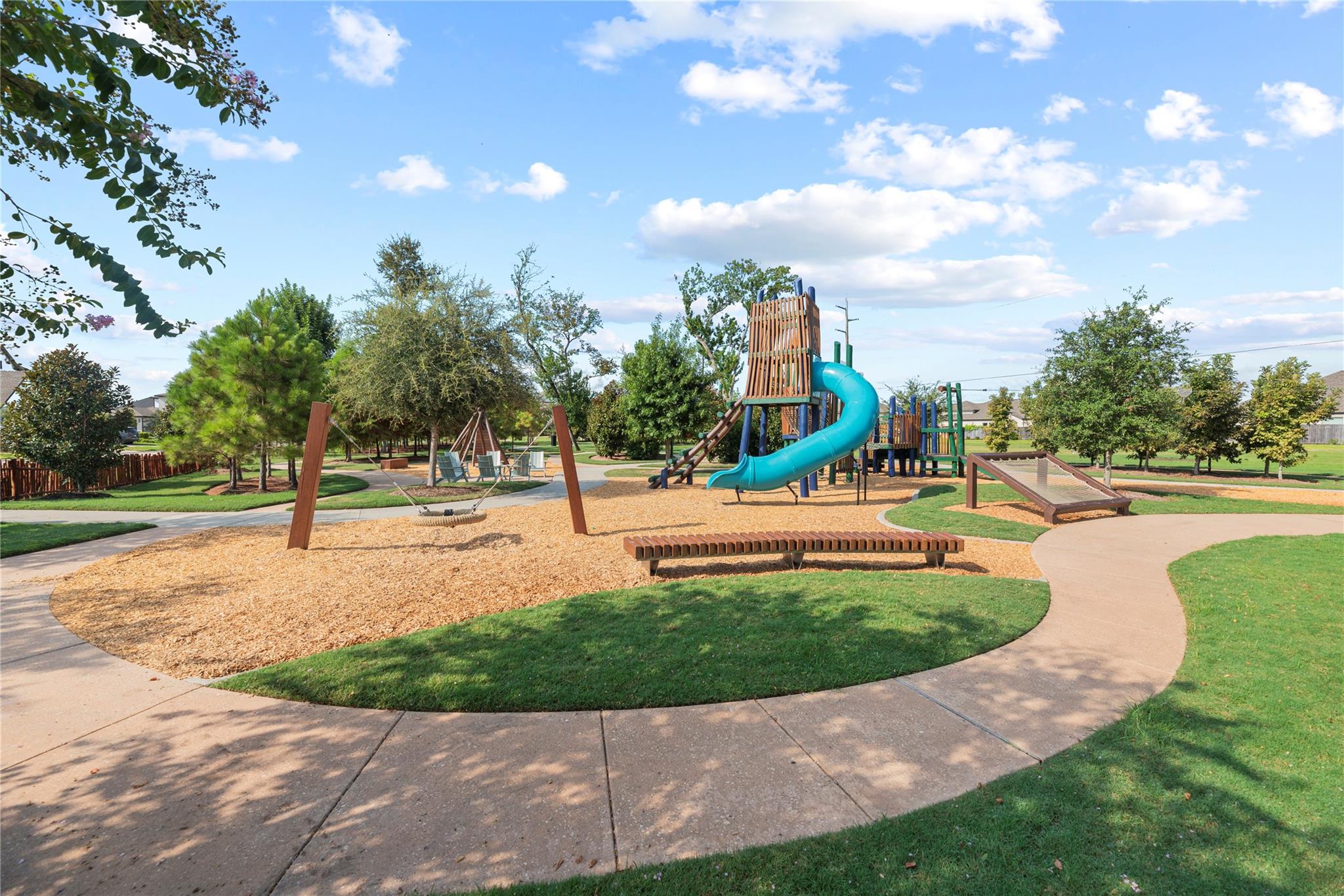 Neighborhood playground with a turquoise spiral slide, swings, seesaw, and shaded walking paths.