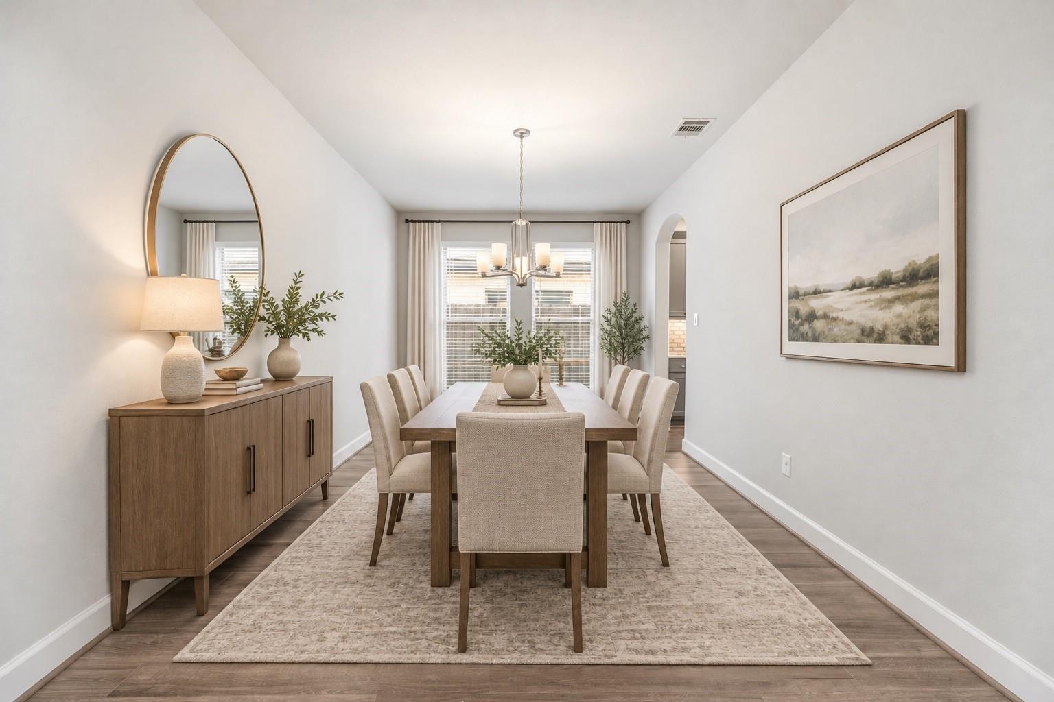 Dining room with a long wooden table, upholstered chairs, and a wood sideboard beneath an oval mirror.