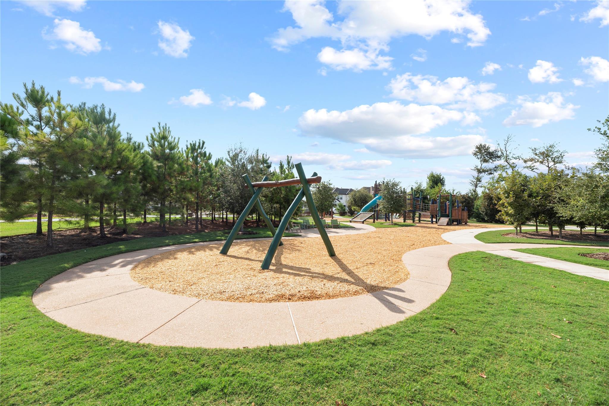Community playground with a wood-chip play area, climbing structure, slide, and curving paths.