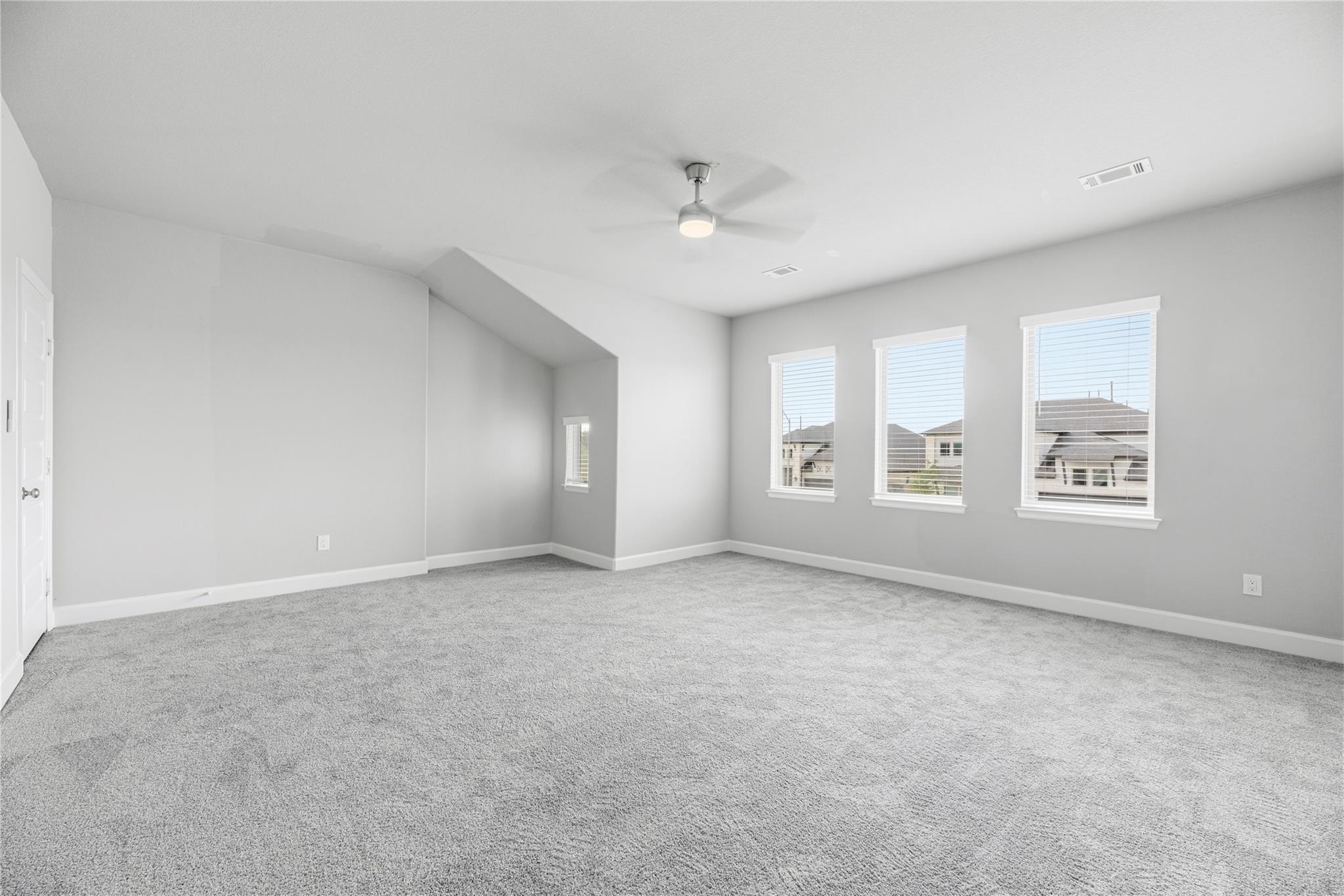 Empty carpeted bedroom with three windows and a ceiling fan.