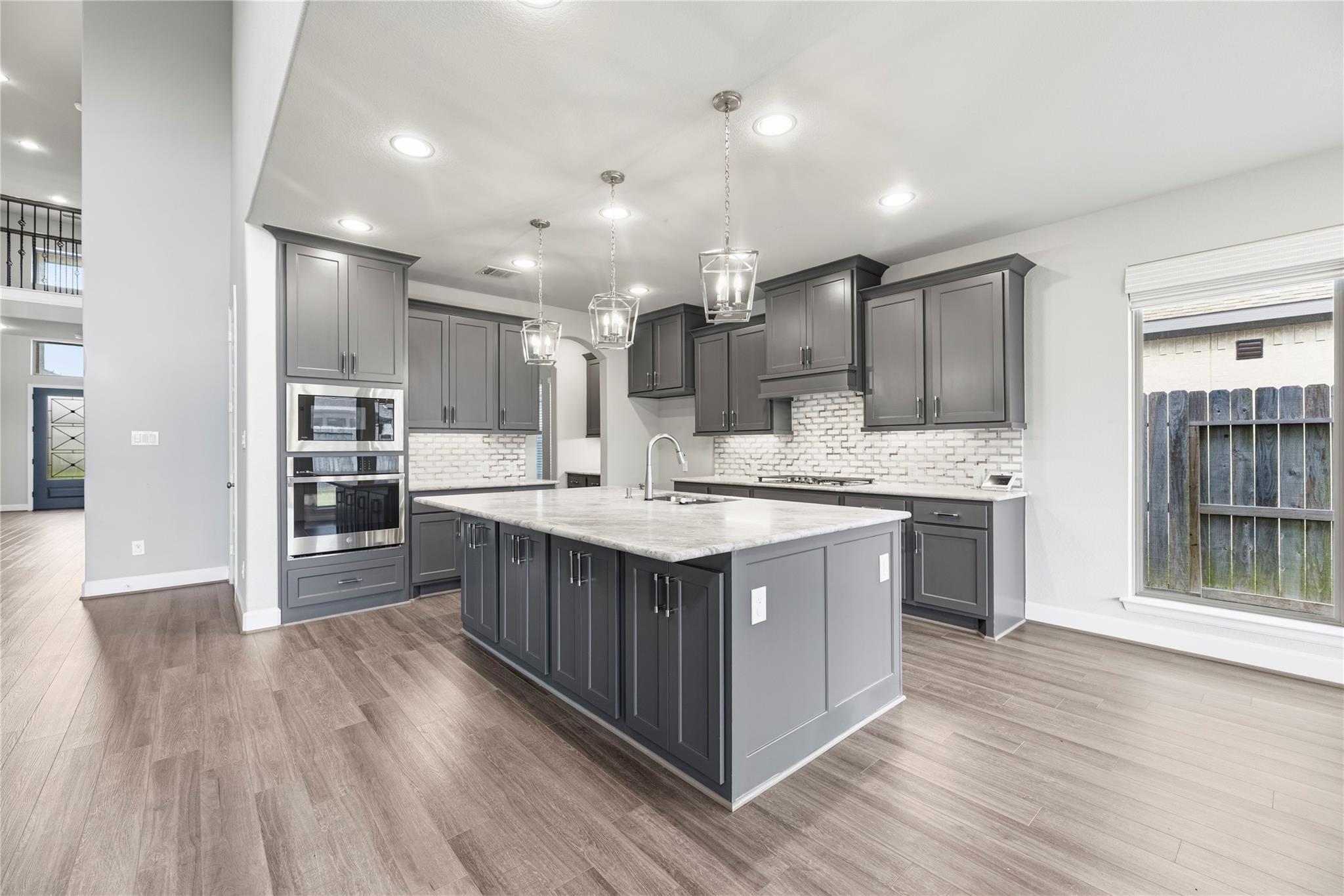 Kitchen with a large marble-look island, dark gray cabinets, white brick backsplash, and three pendant lights.