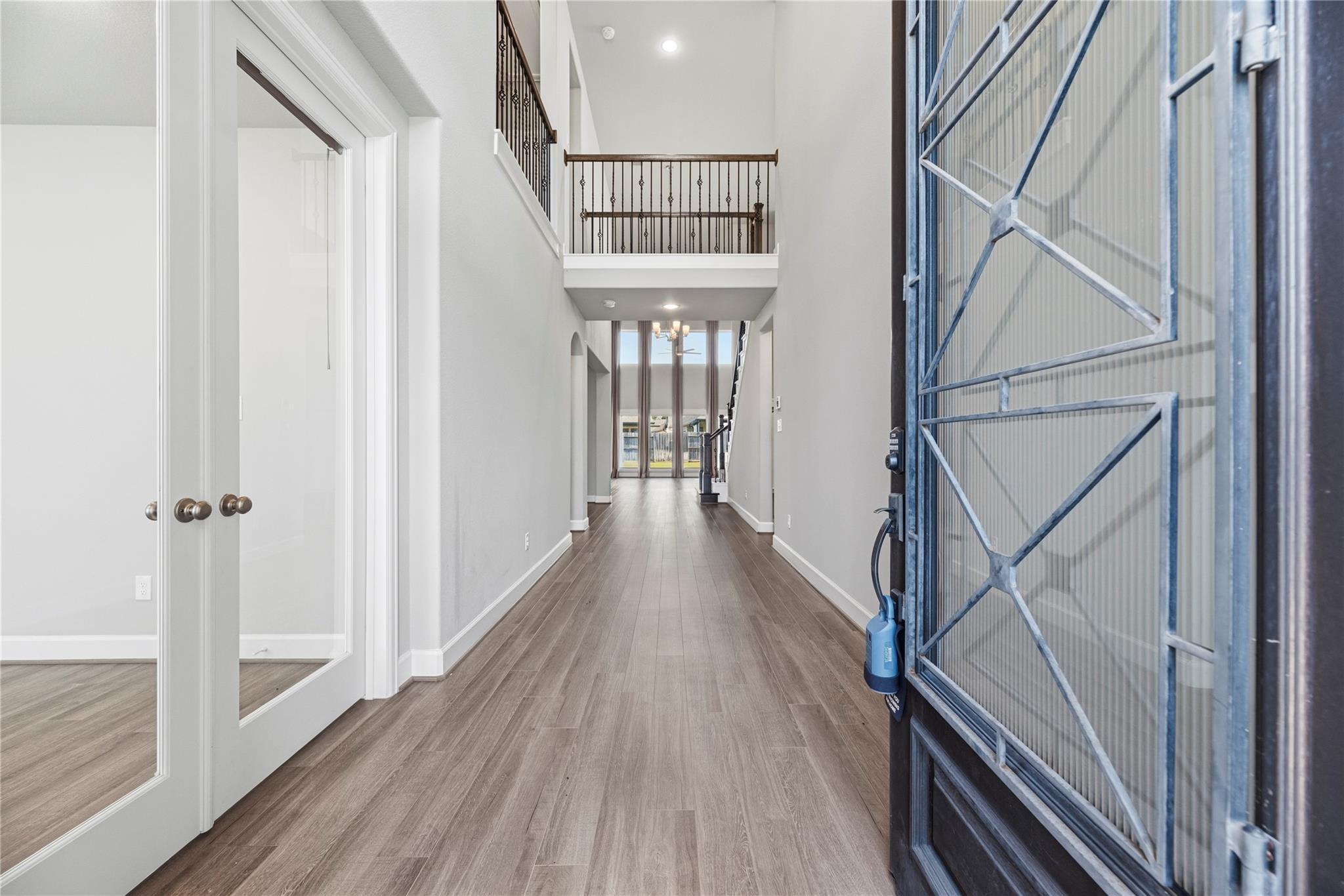 Two-story entry hall with wood-look flooring, an open upstairs landing, and a decorative metal front door.