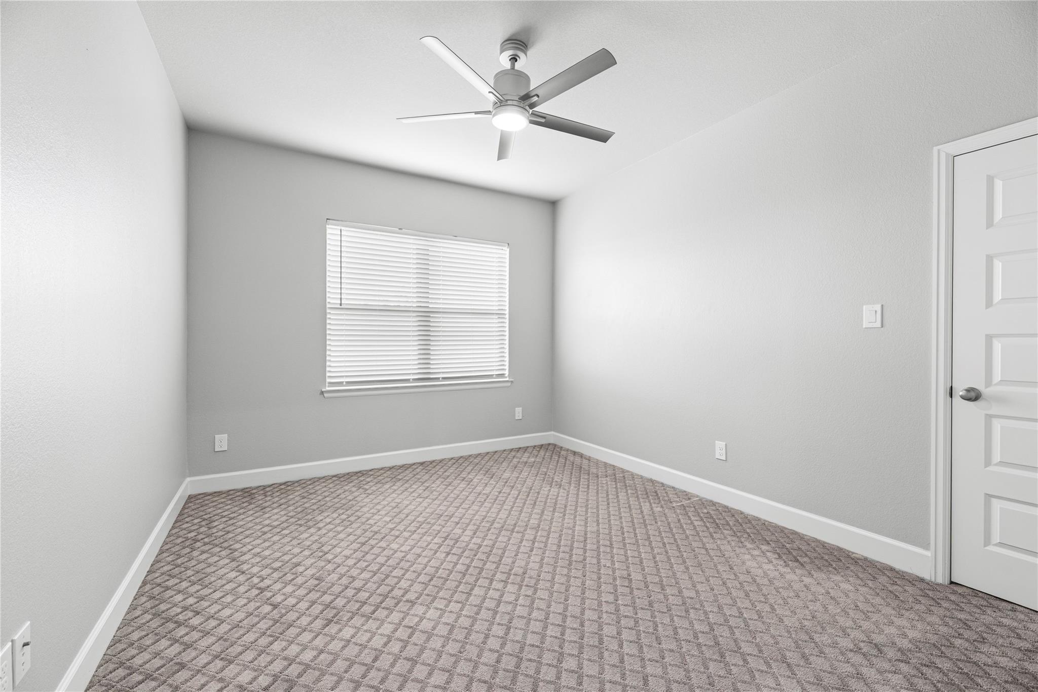 Empty bedroom with patterned carpet, a window with blinds, and a ceiling fan.
