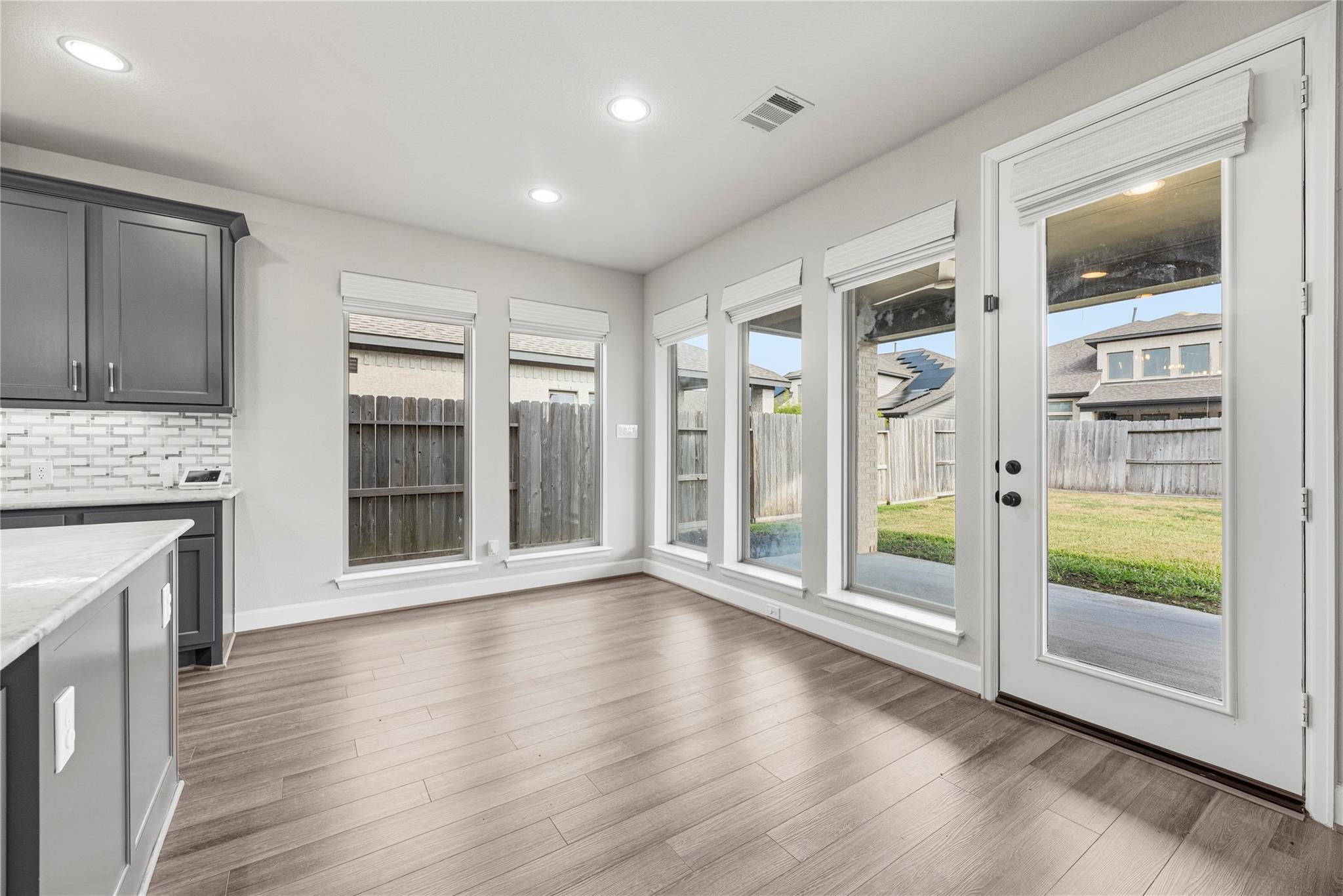 Kitchen dining area with gray cabinets, wood-look floors, and windows overlooking the backyard.