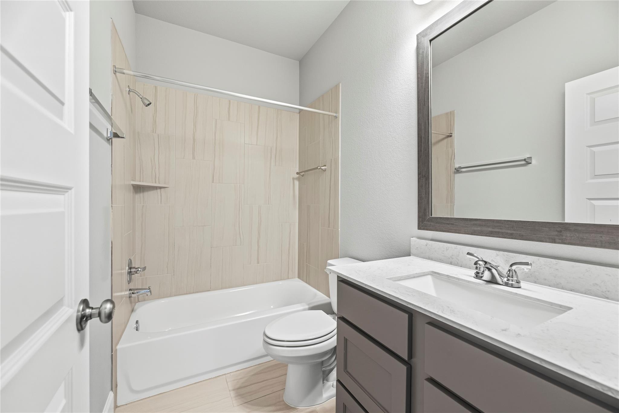 Bathroom with a beige tiled tub surround, white bathtub, and gray vanity with a large framed mirror.