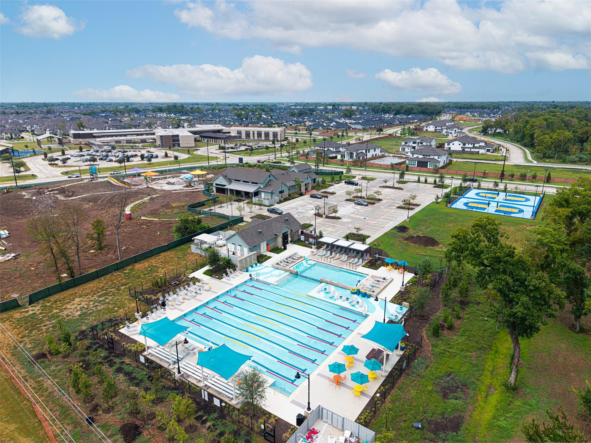 Aerial view of a residential community with a large swimming pool, shaded seating, and a basketball court.