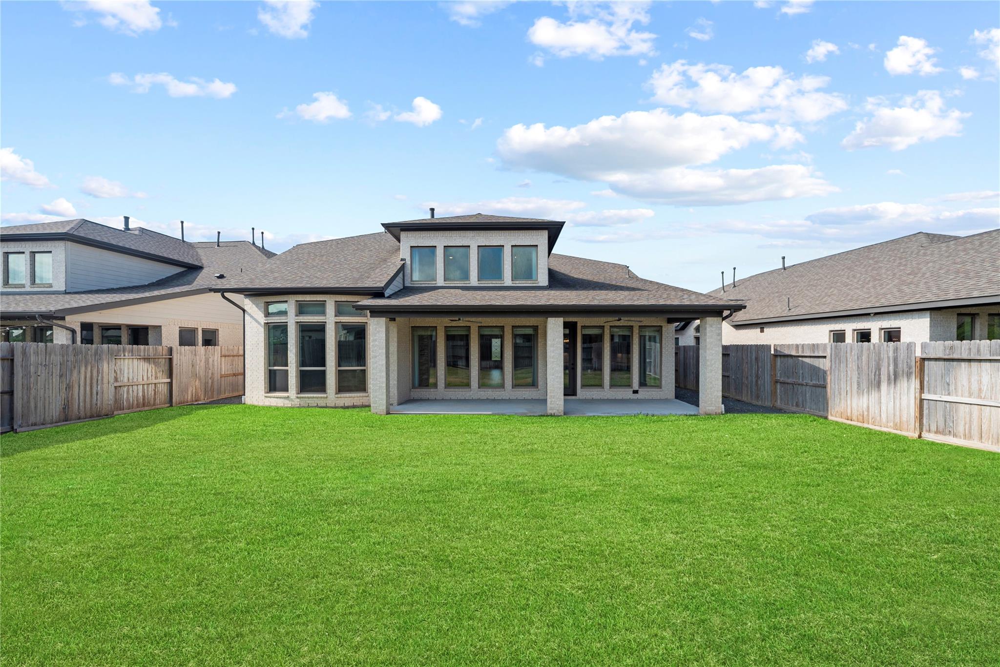 Rear of a two-story house with a covered patio, broad lawn, and wooden privacy fences.