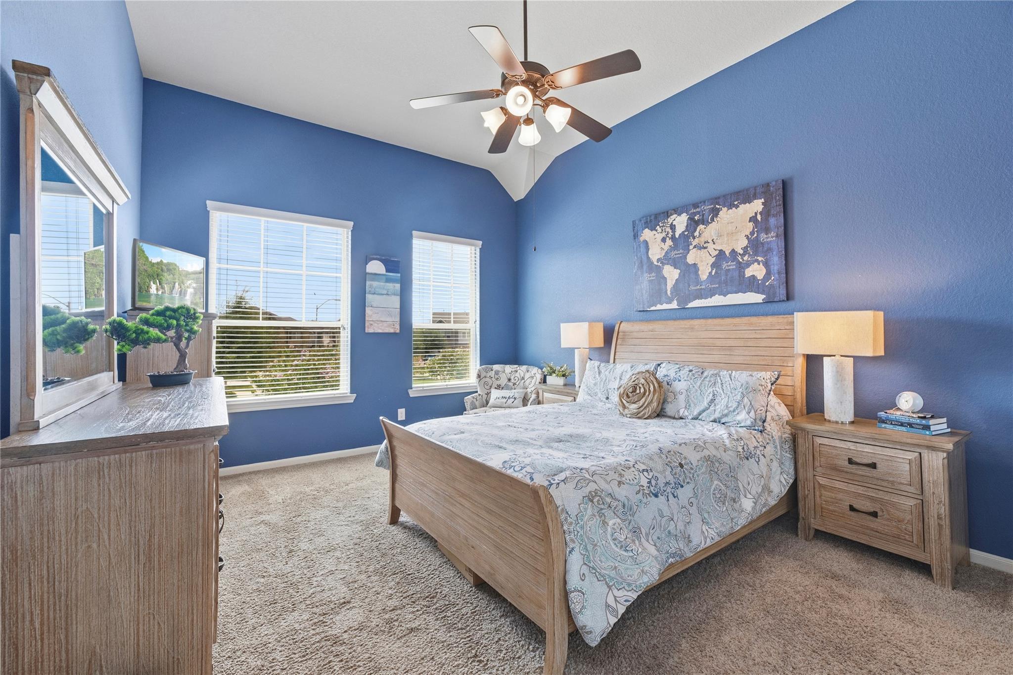 Blue bedroom with a wooden bed, patterned bedding, ceiling fan, and windows with white blinds.
