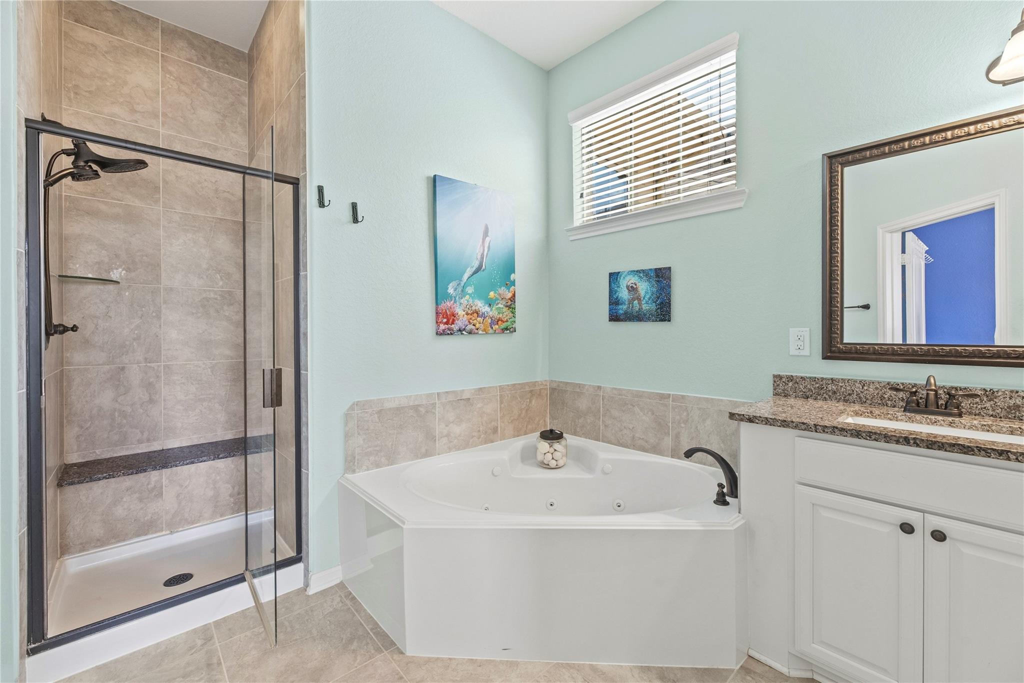 Bathroom with tiled glass shower, corner jetted tub, and granite vanity.