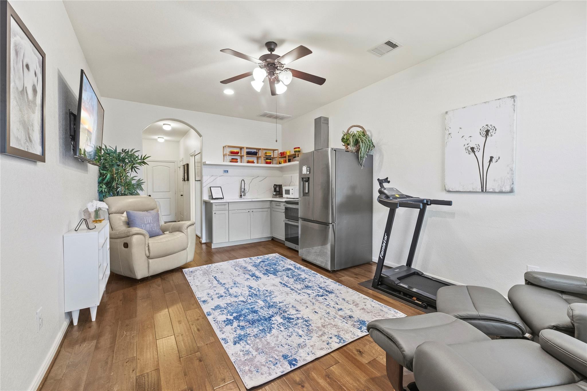 Furnished living area with a compact kitchen, treadmill, recliner, and blue-and-white rug.