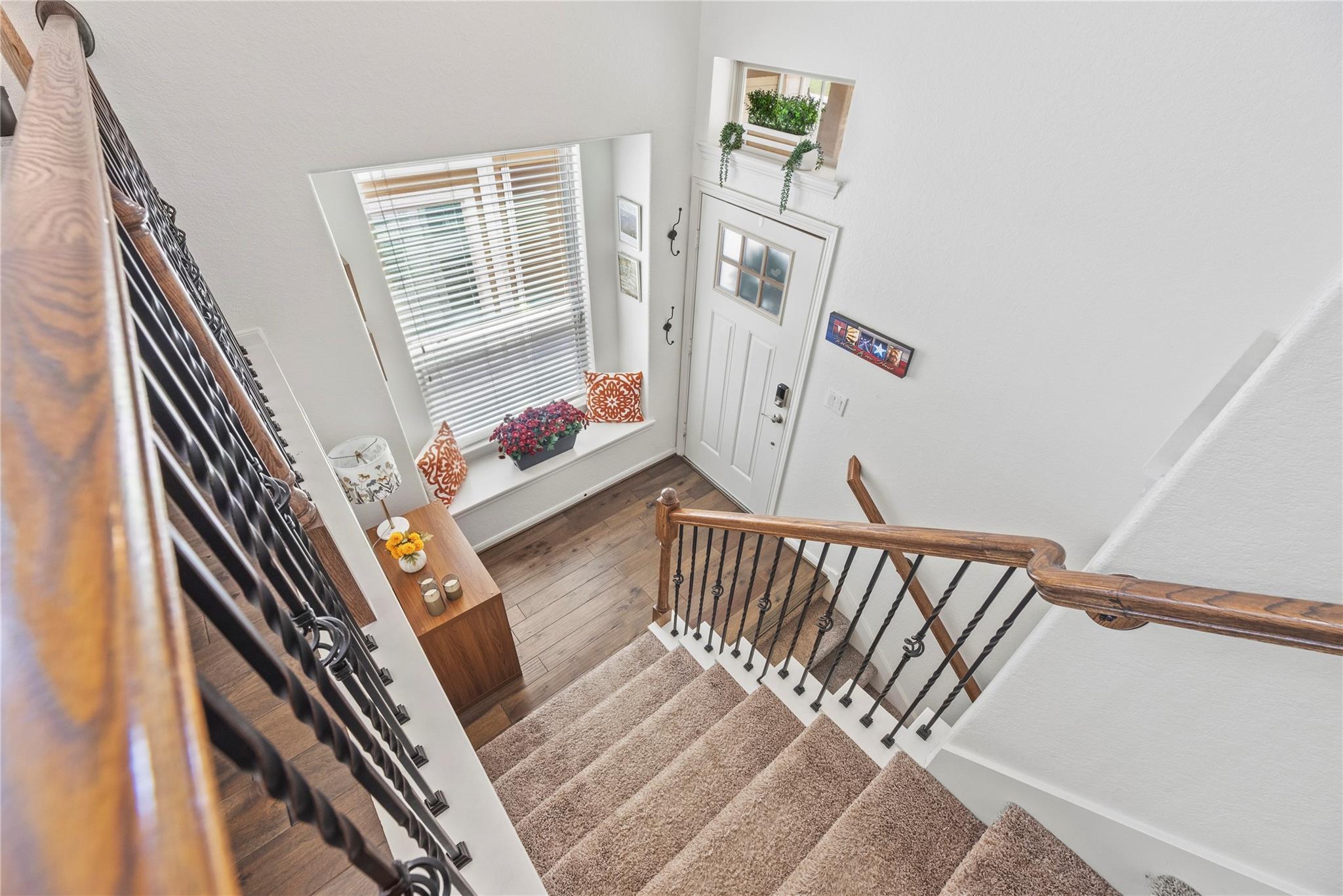 Two-story entry foyer with carpeted stairs, wood handrails, iron balusters, and a bright window beside the front door.
