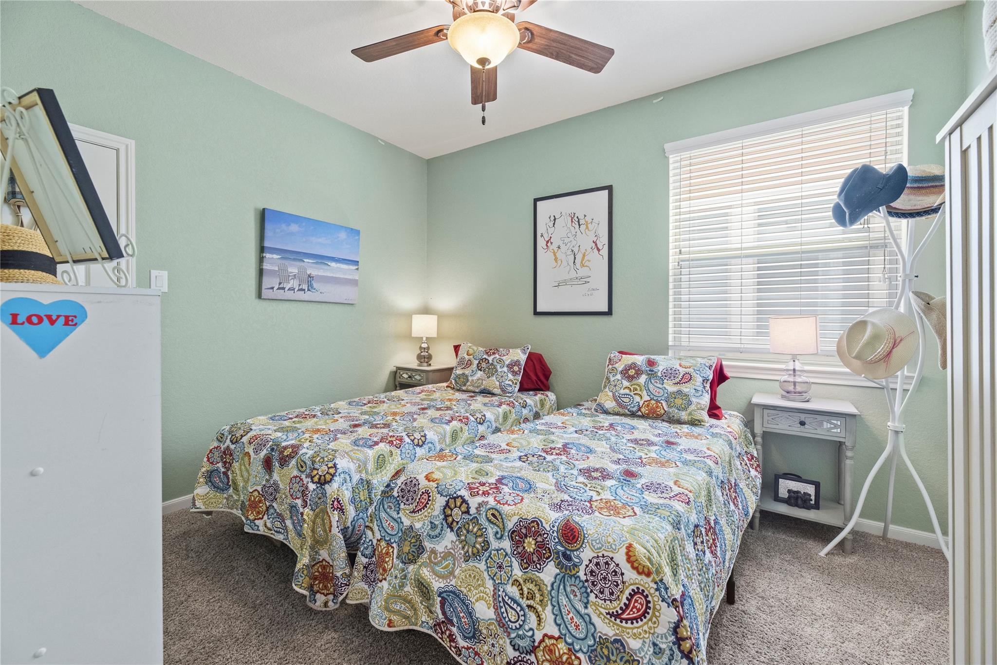Bedroom with two twin beds in colorful patterned bedding and a white hat stand.