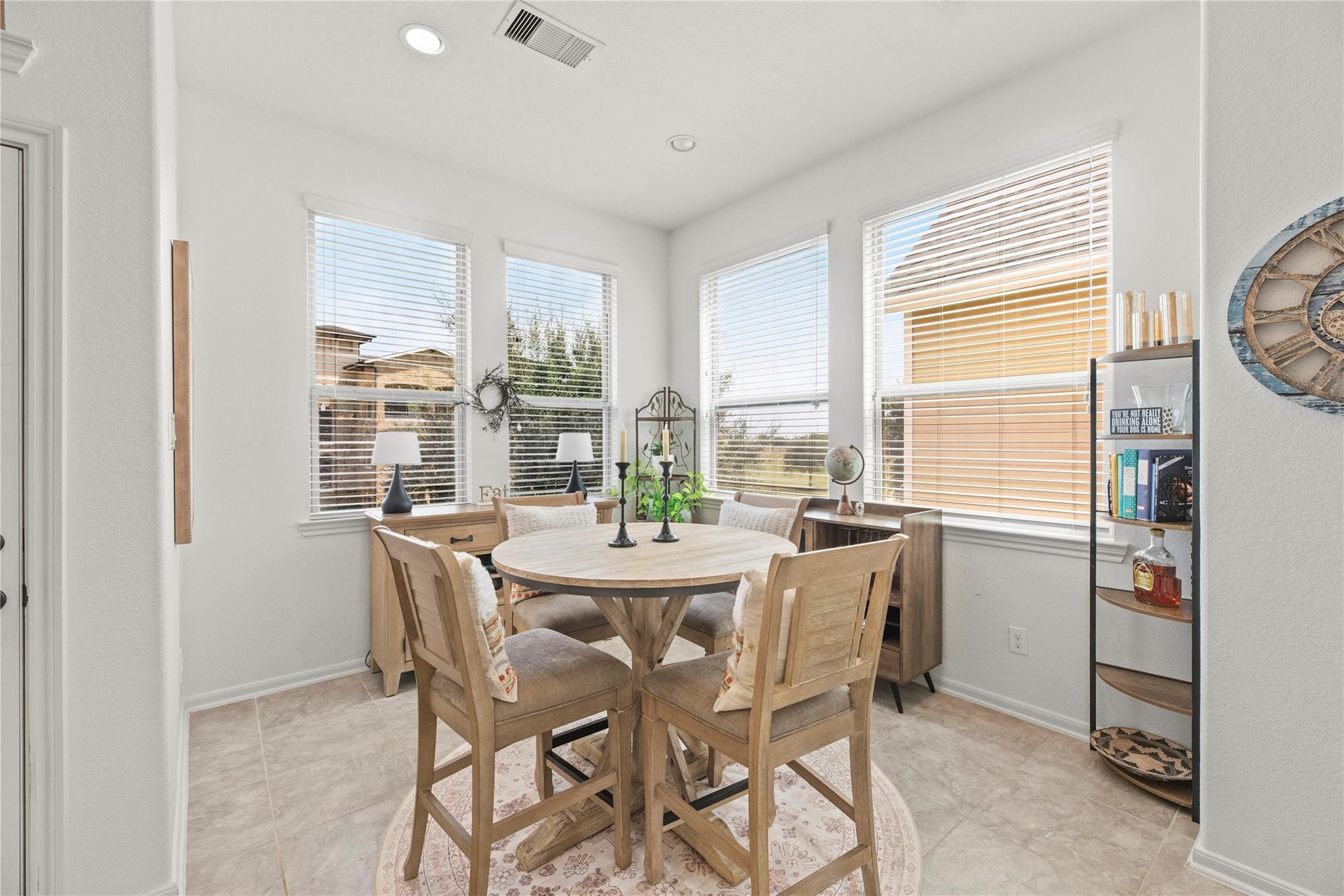 Dining nook with a round wood table, four chairs, and large windows with blinds.