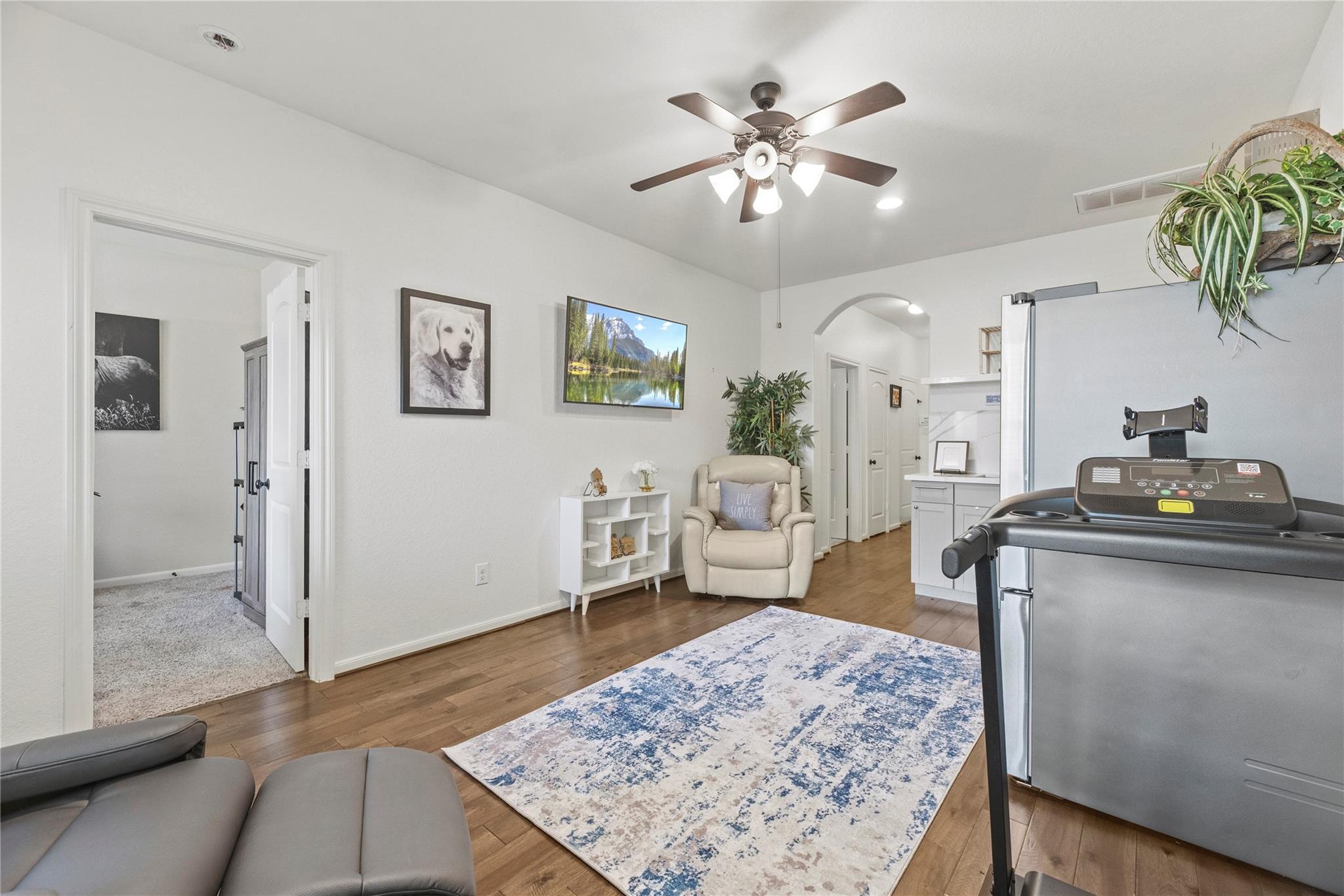 Home workout room with a treadmill, patterned rug, wood floors, and an adjoining kitchen.